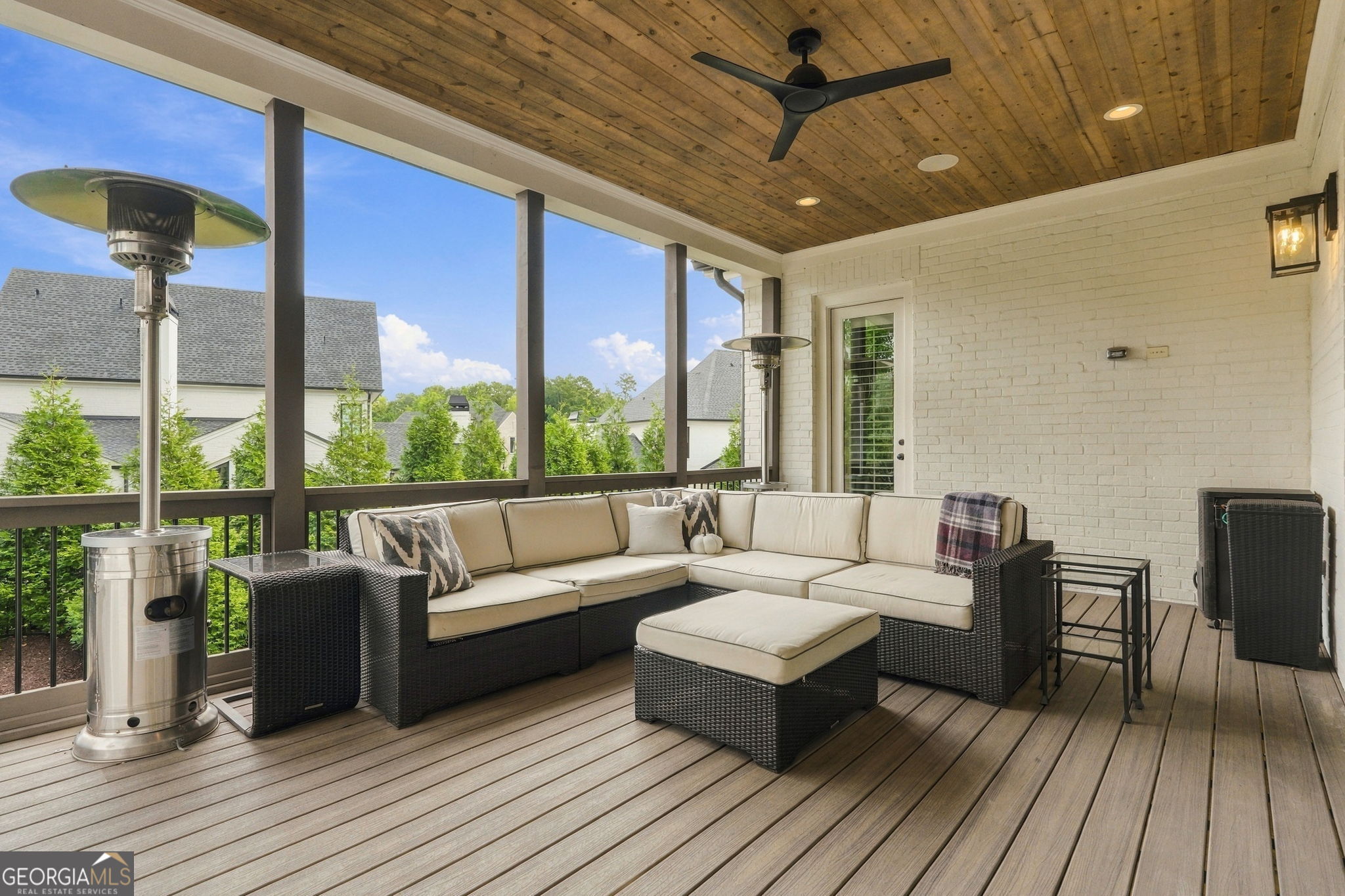 Covered patio with a wood ceiling, sectional sofa, ottoman, and patio heaters.
