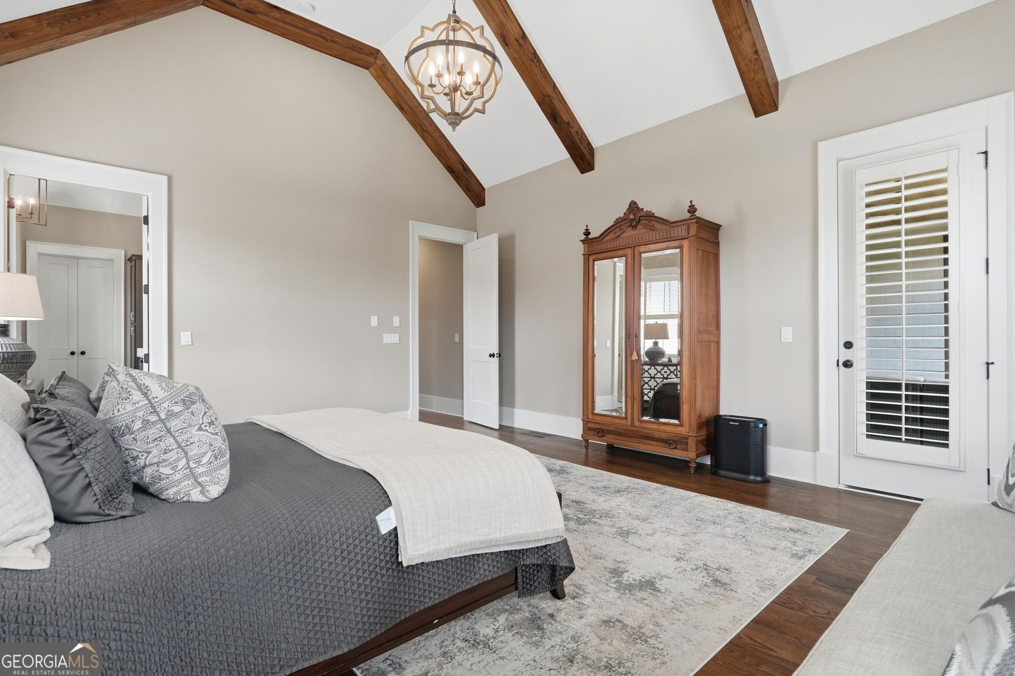 Furnished bedroom with exposed ceiling beams, a gray quilted bed, and a mirrored wooden armoire.