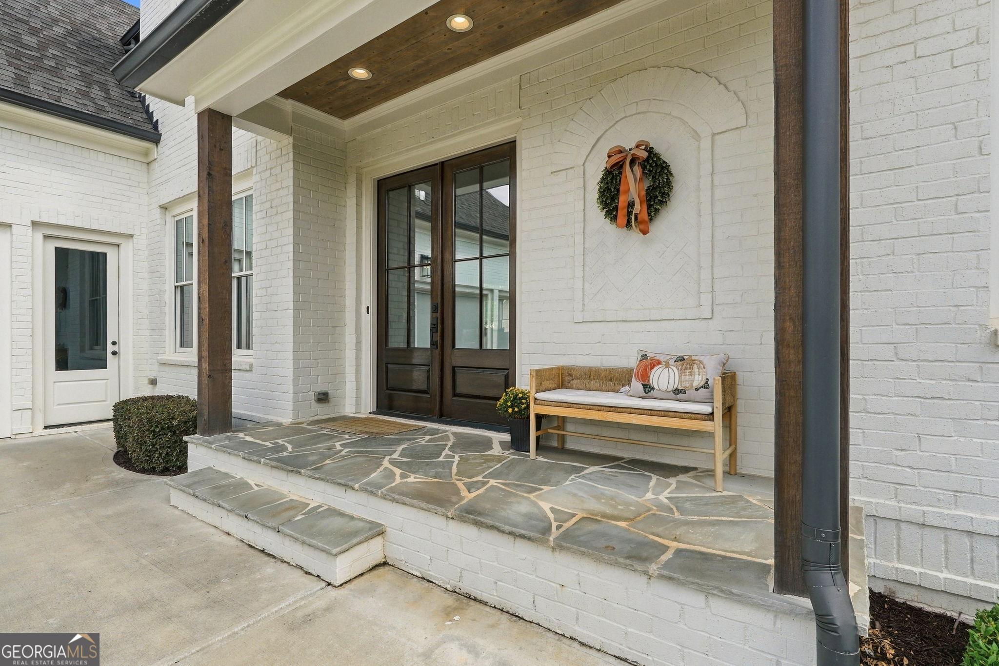 White brick home entrance with dark double doors, a covered stone porch, and a wooden bench.