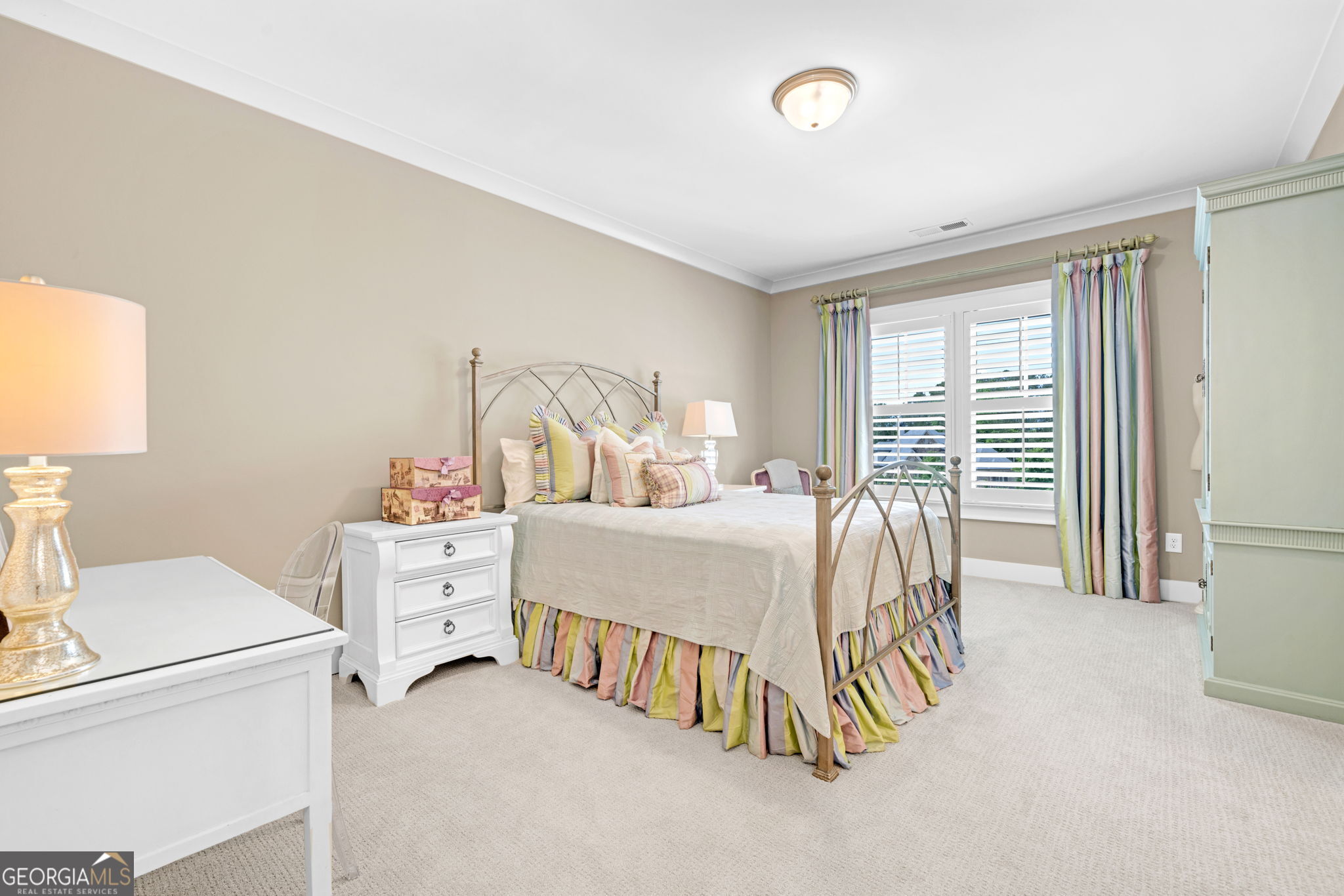 Bedroom with a metal-frame bed, colorful striped bedding, and plantation-shuttered windows.