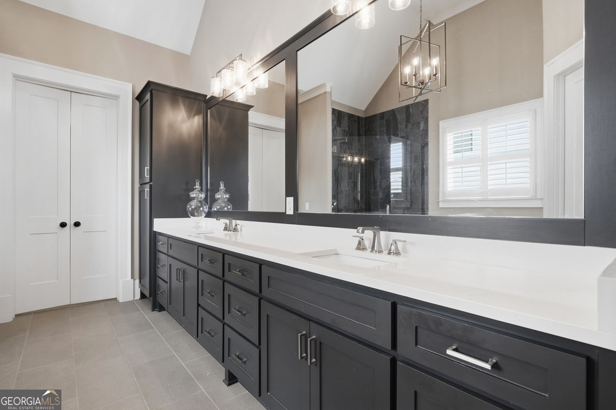 Bathroom with a long double vanity, dark cabinetry, and a mirror reflecting a tiled shower.
