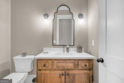 Bathroom with rustic wood vanity, white countertop, arched mirror, and toilet.