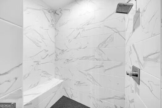 Walk-in shower with white marble-look tile, a square showerhead, and dark linear drain.