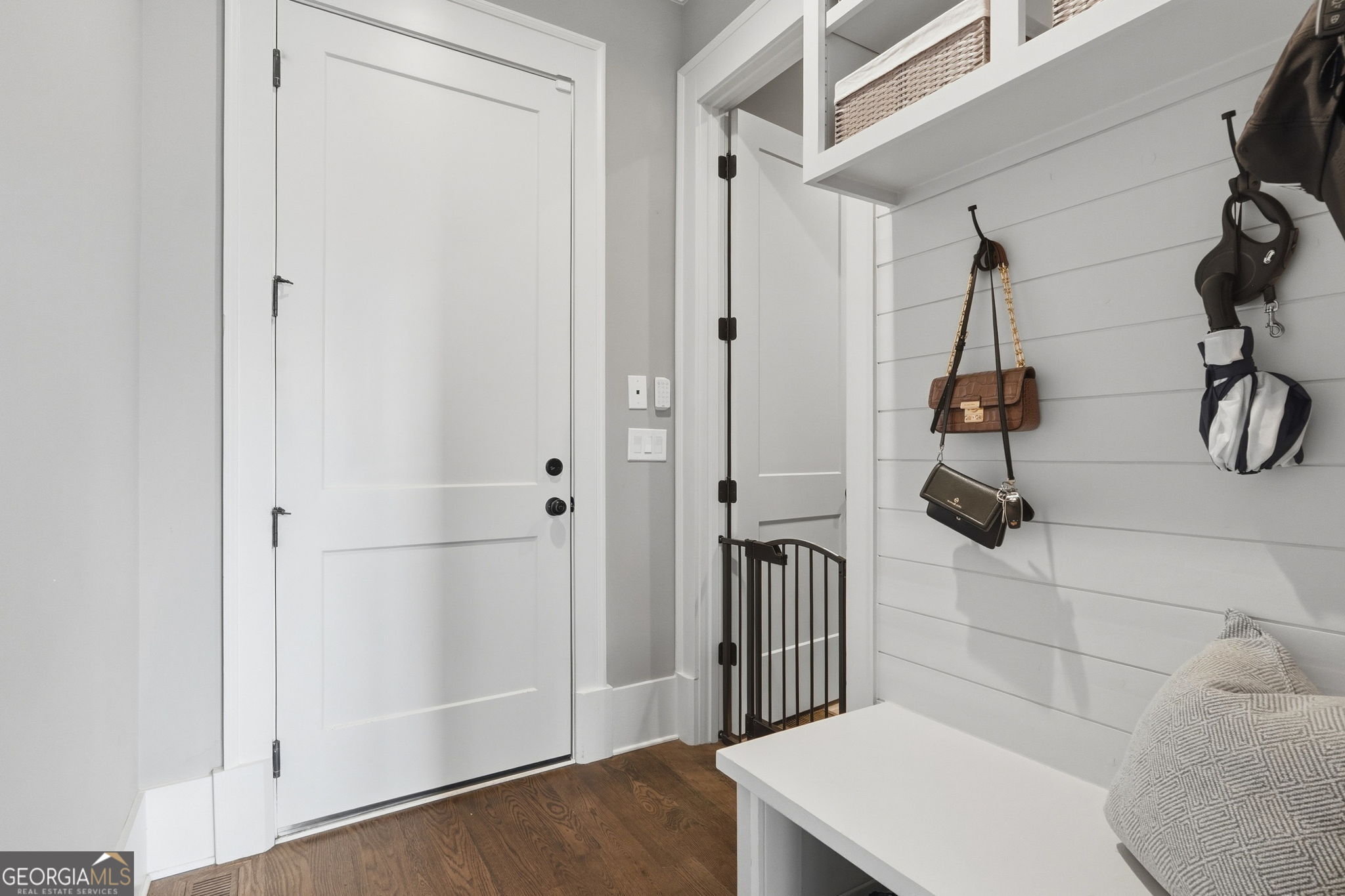 White entryway with a built-in bench, overhead basket storage, and hooks for bags and an umbrella.