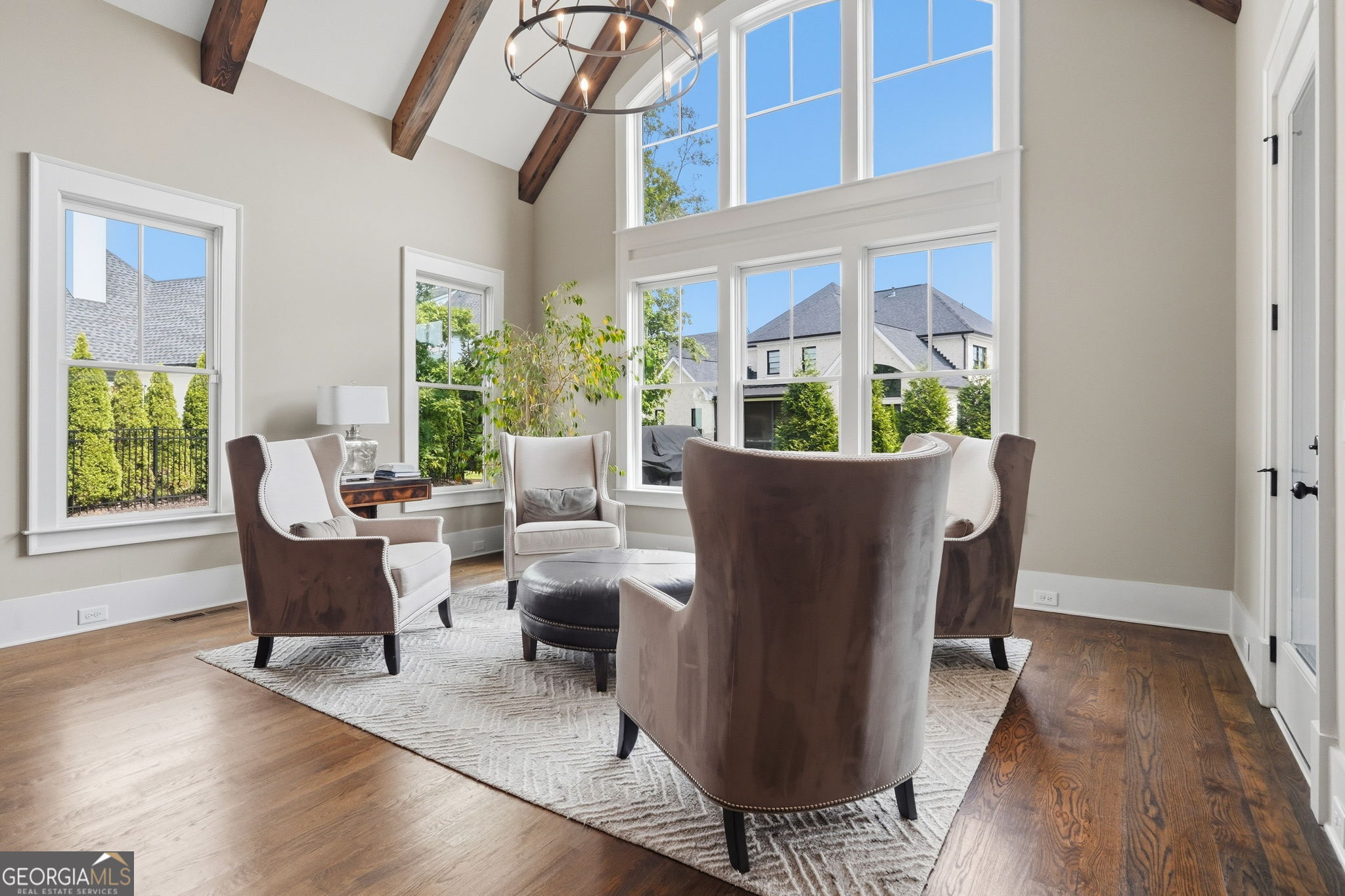 Furnished sitting room with exposed wood beams, tall windows, and upholstered armchairs.