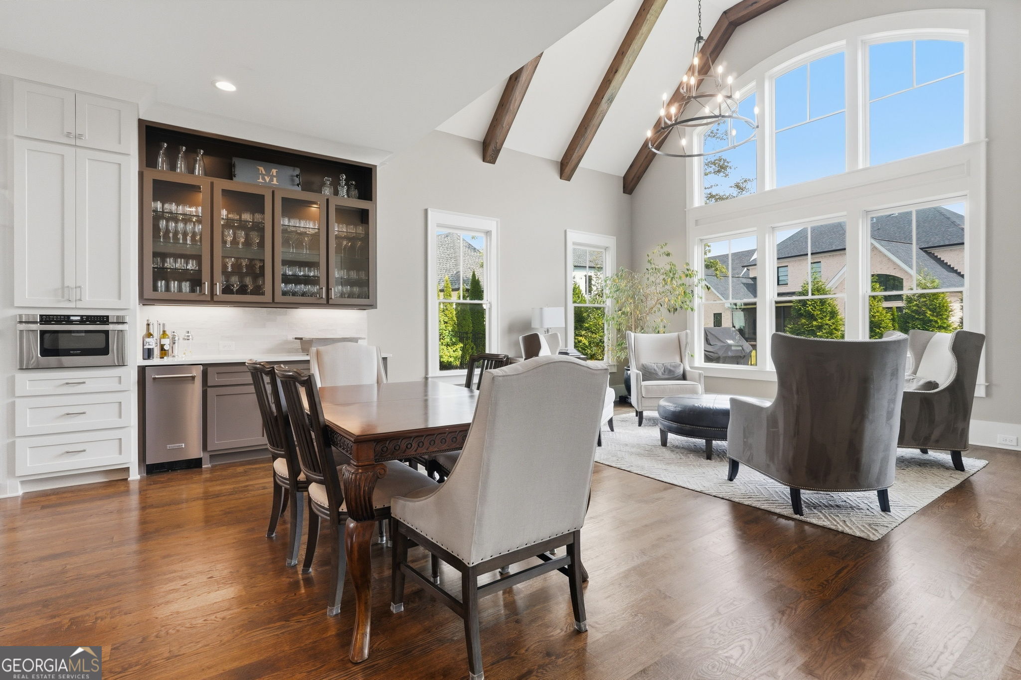 Open dining and sitting area with exposed ceiling beams, a built-in bar, and large windows.