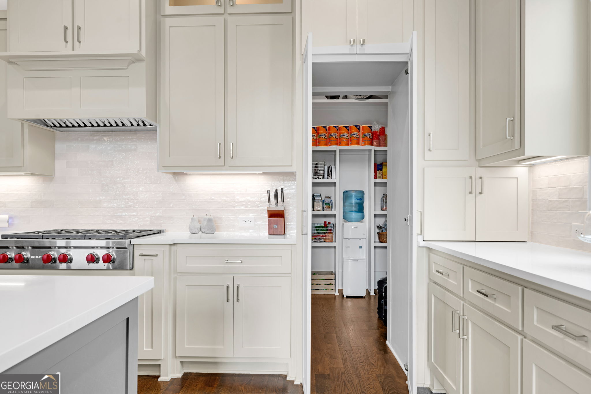 White kitchen with a gas range and open, well-stocked pantry.