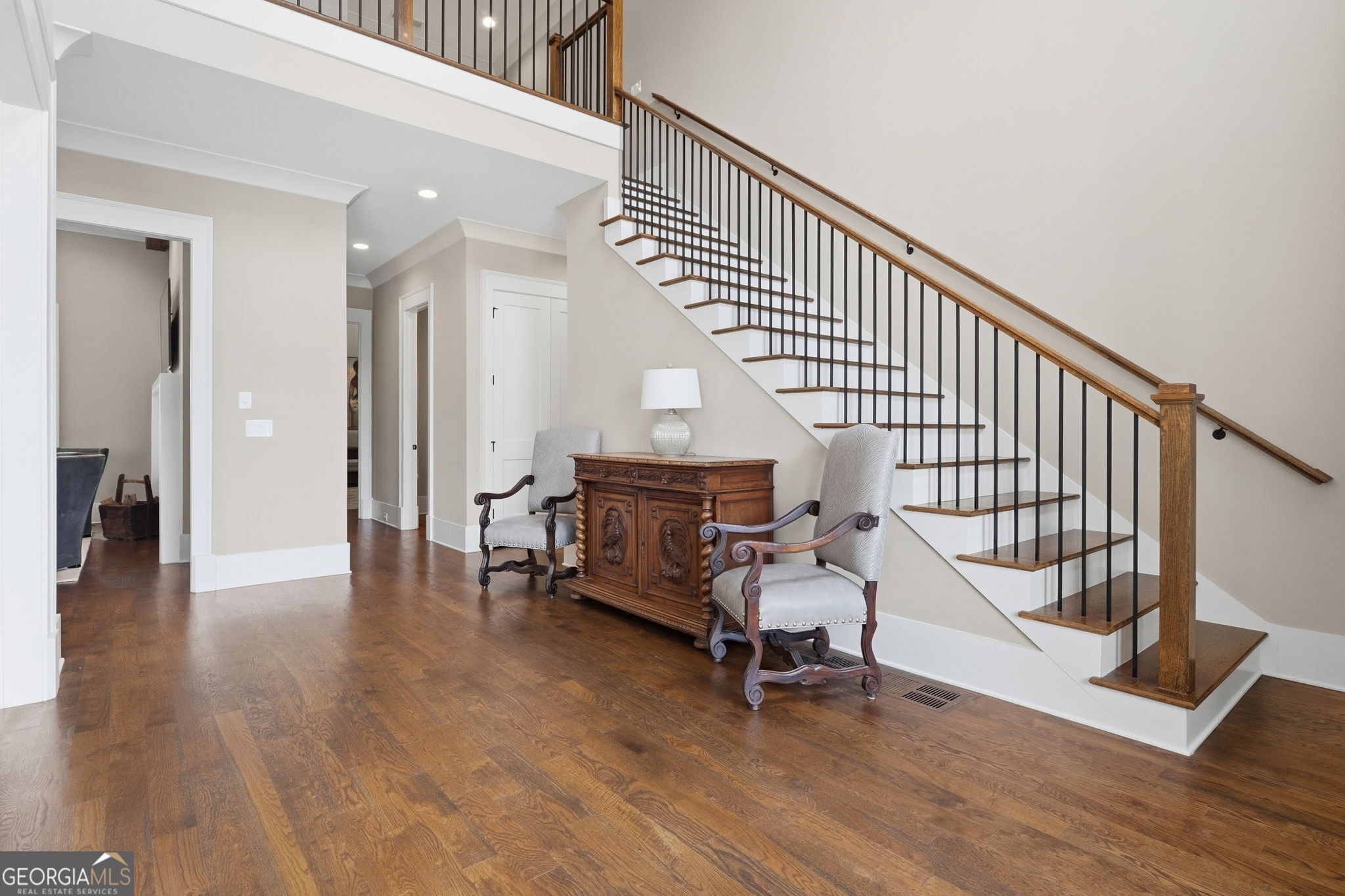 Foyer with a wood-and-metal staircase, hardwood floors, and a sitting area beneath the stairs.