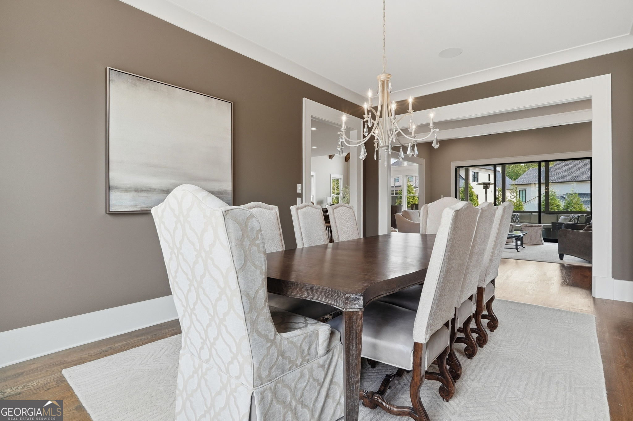 Furnished dining room with a dark wood table, pale upholstered chairs, and a crystal chandelier.