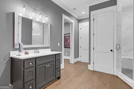 Bathroom with a dark vanity, wide mirror, wood-look flooring, and glass-enclosed shower.