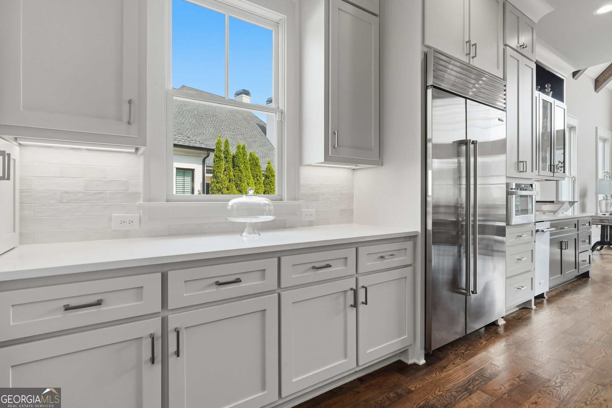 Bright kitchen with white cabinetry, stainless steel appliances, a large window, and dark hardwood floors.
