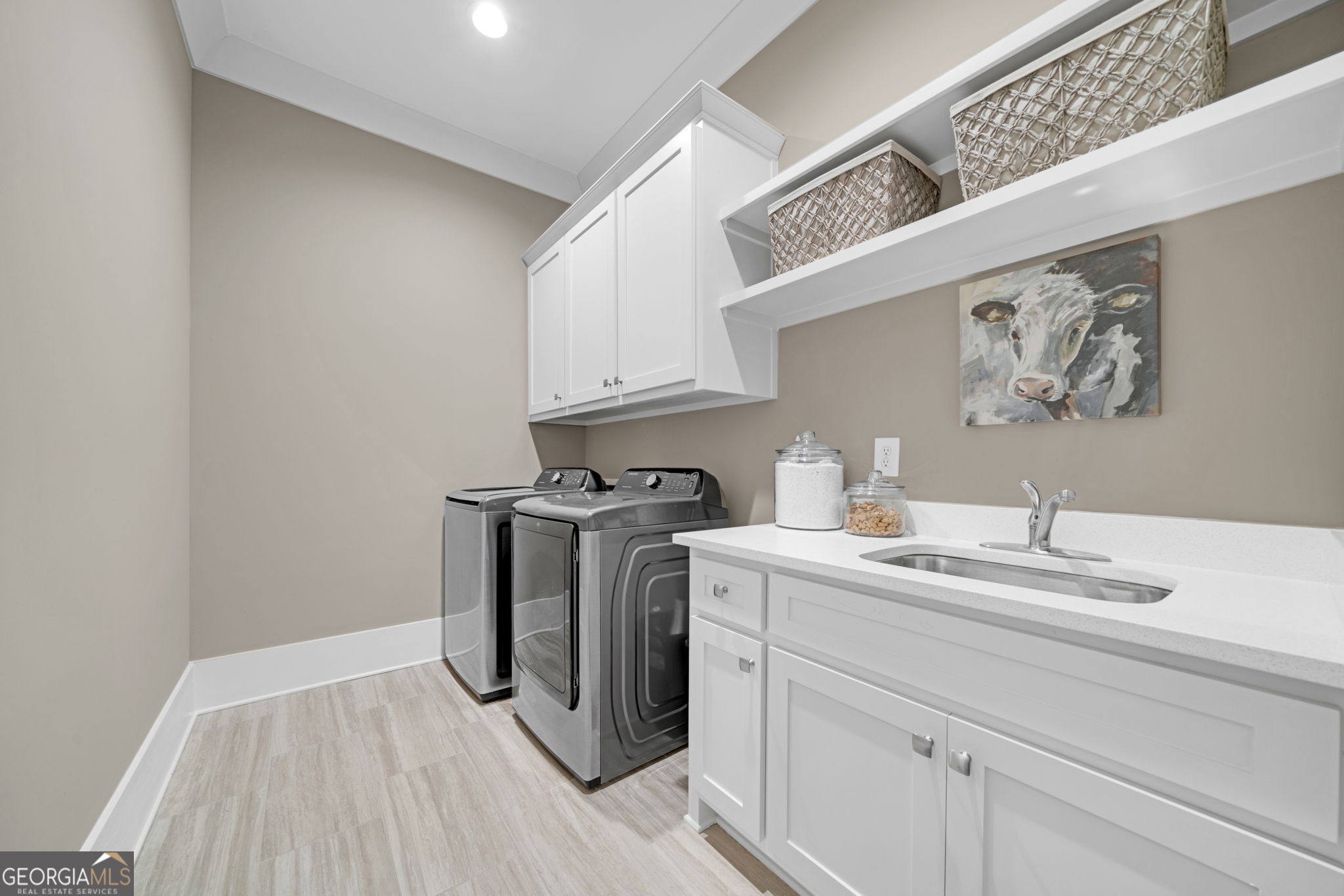 Laundry room with washer and dryer, white cabinets, countertop sink, and open storage shelves.