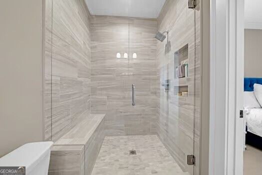 Walk-in shower with light tile, built-in bench, recessed niches, and frameless glass door.