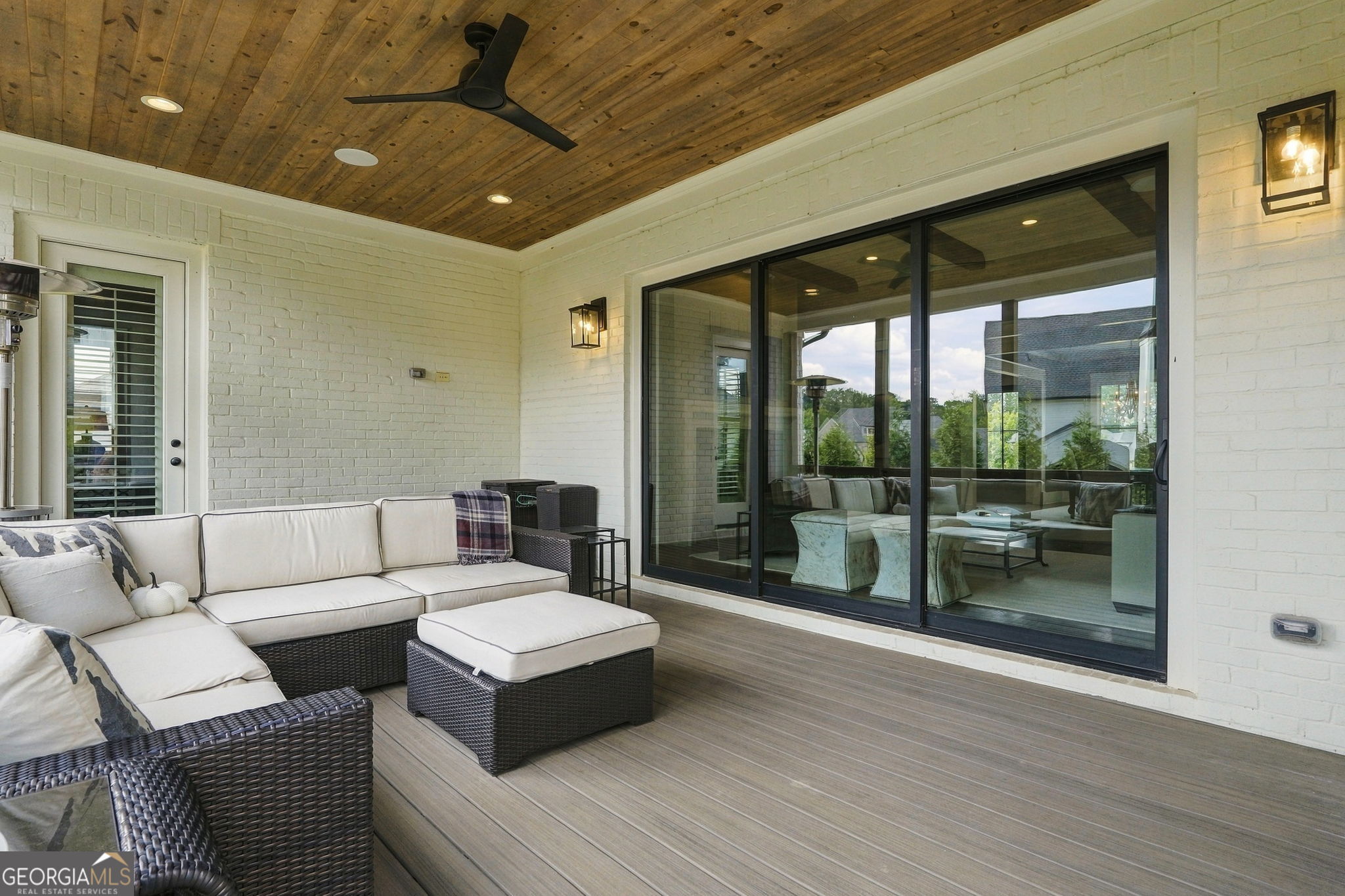 Covered patio with a wood-plank ceiling, wicker sectional, and large sliding glass doors.