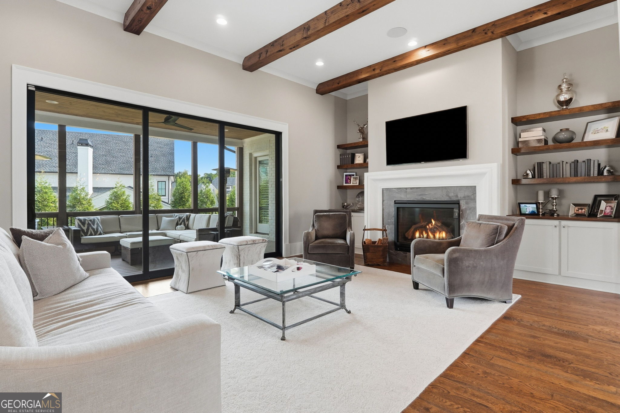 Living room with exposed wood beams, a lit fireplace, and sliding doors to a covered patio.