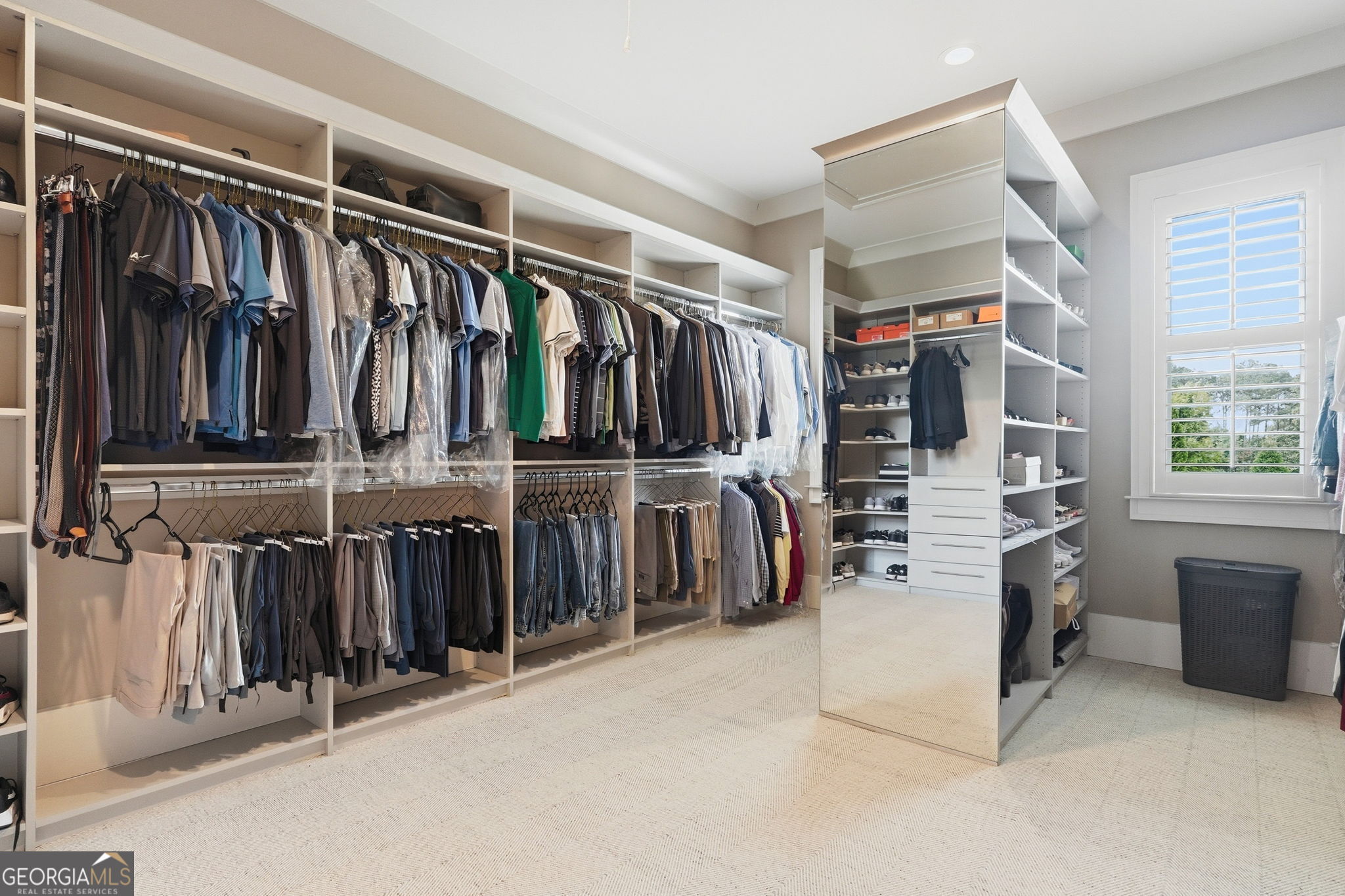Walk-in closet with extensive clothing storage, a mirrored shelving unit, and a shuttered window.