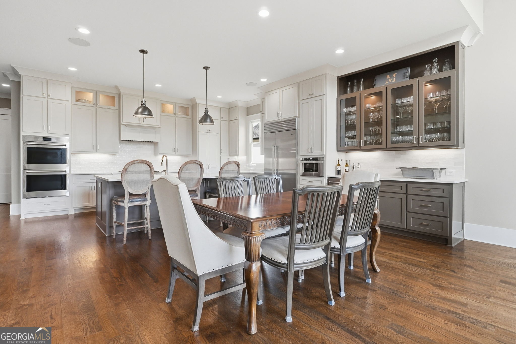 Kitchen and dining area with white cabinets, stainless appliances, glass-front bar storage, and a large wooden table.