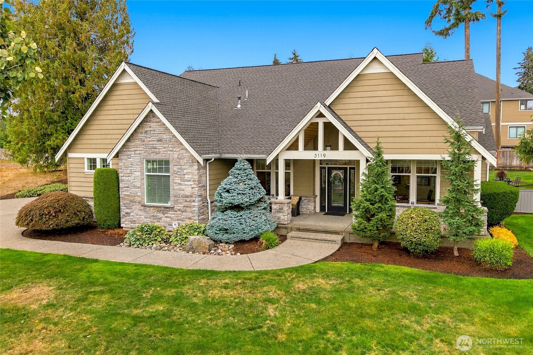Tan and stone house with a gabled roof, landscaped front yard, and curved walkway.