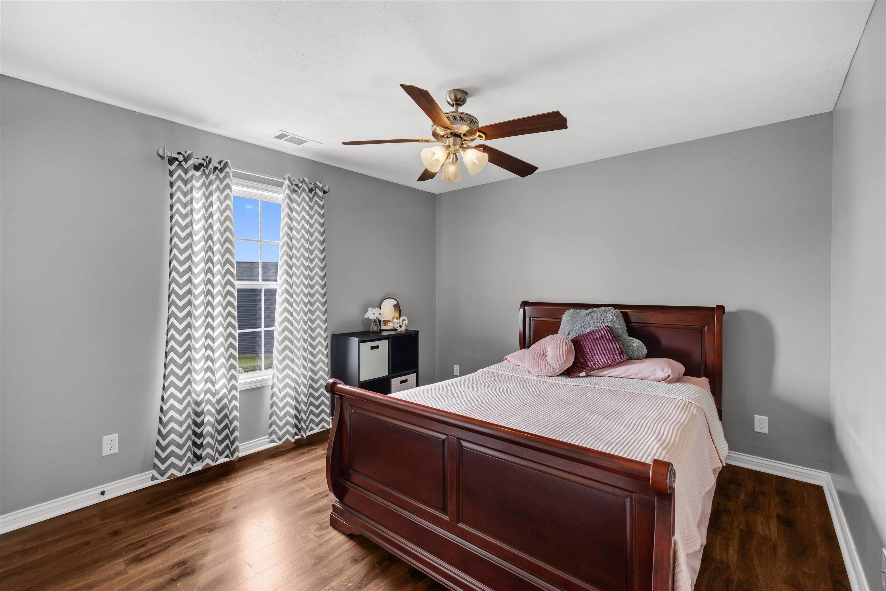 Bedroom with a dark wood bed, pale pink bedding, and chevron curtains framing a tall window.