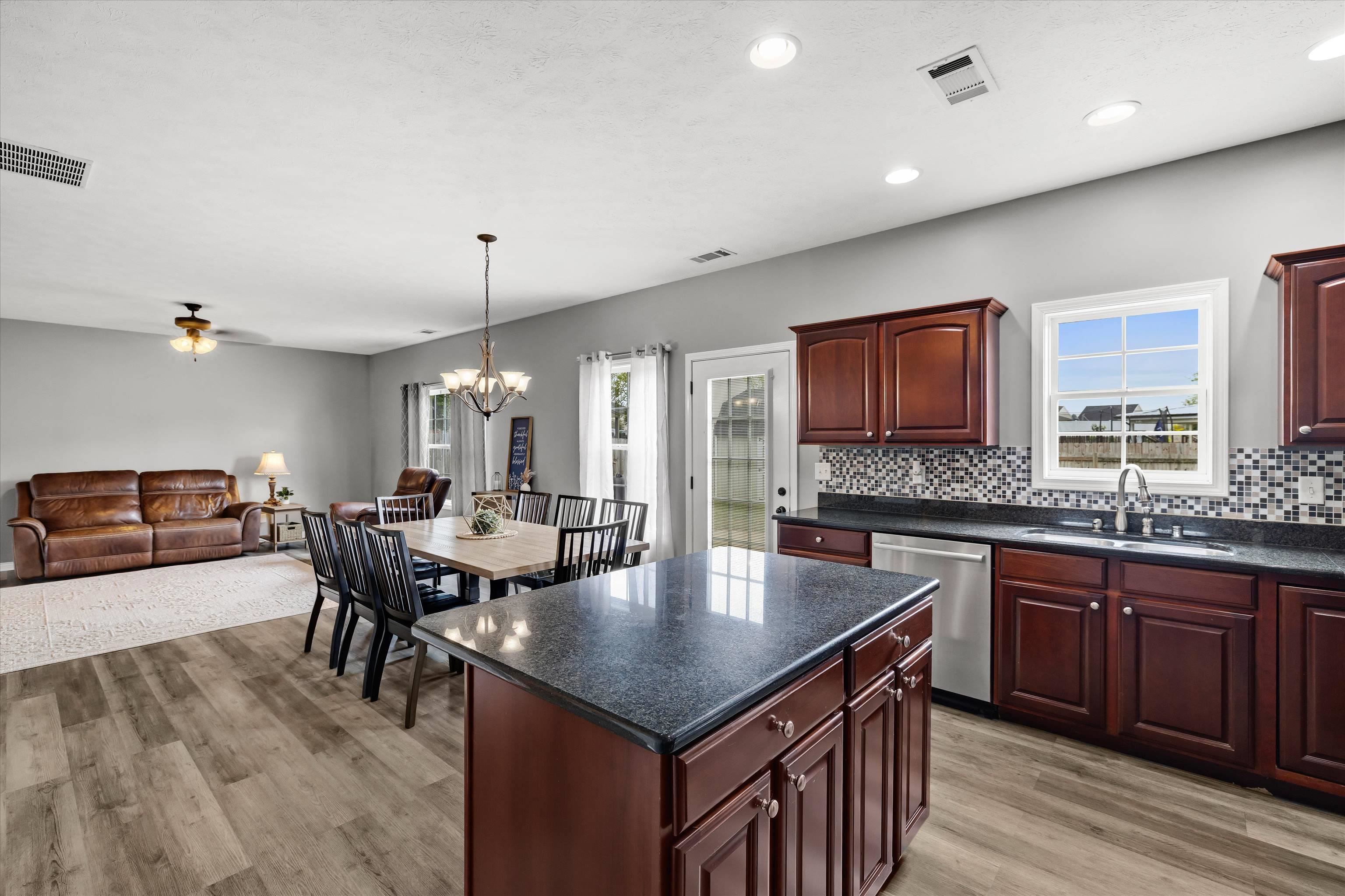 Open-plan kitchen with dark cabinets and granite island, adjoining a dining area and living room.