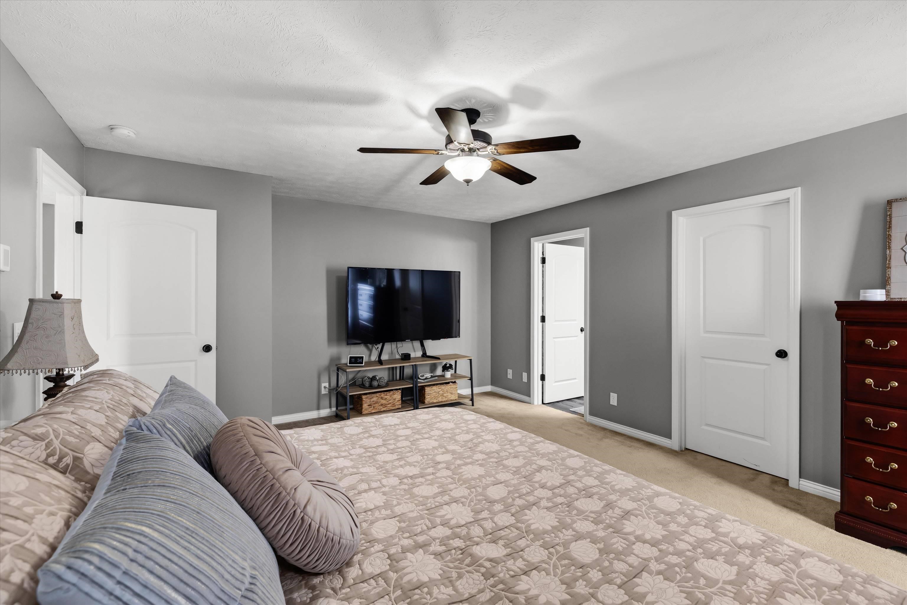 Bedroom with a floral bedspread, ceiling fan, and wall-mounted television