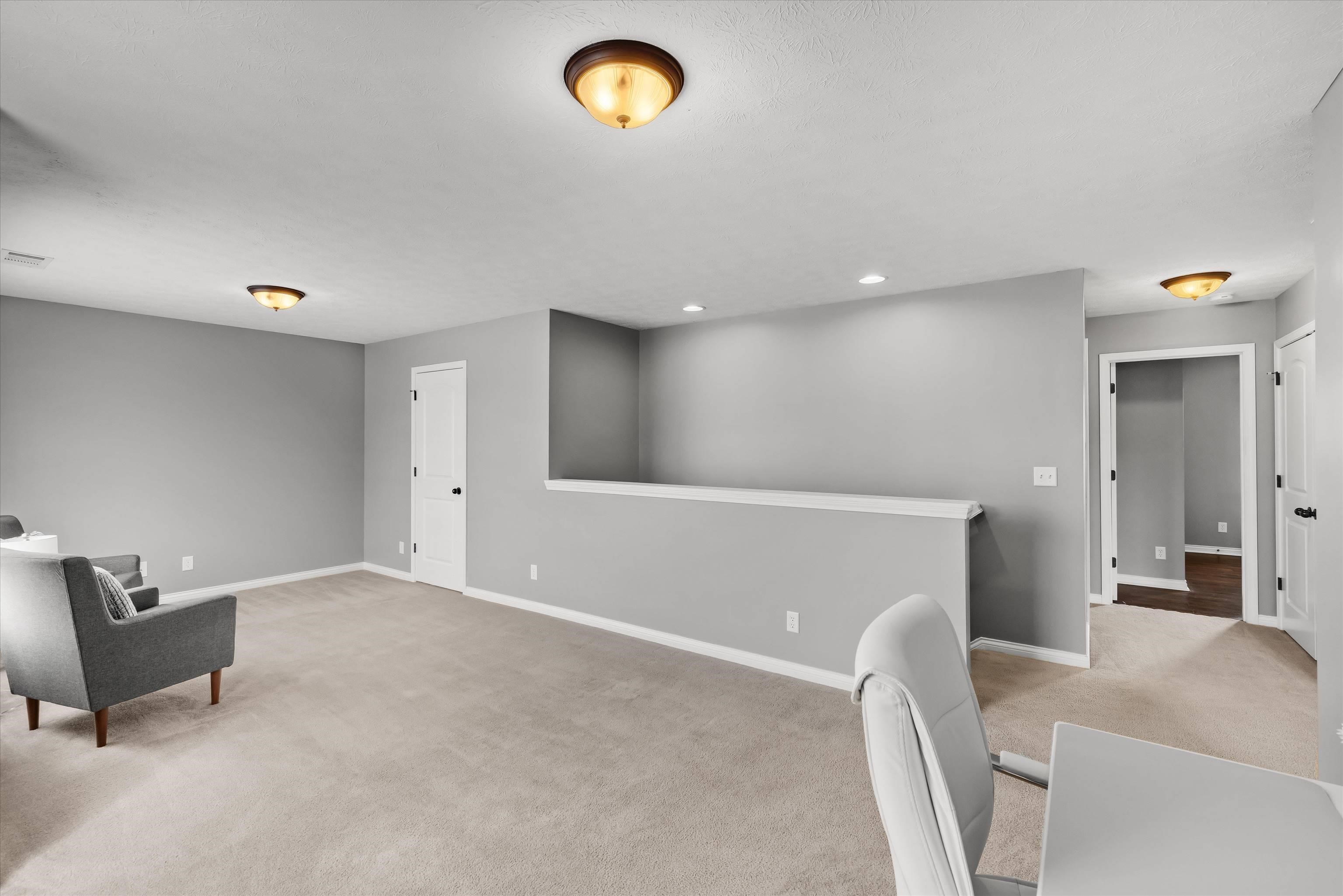 Carpeted living area with gray walls, a white half wall, and doorways to adjoining rooms.