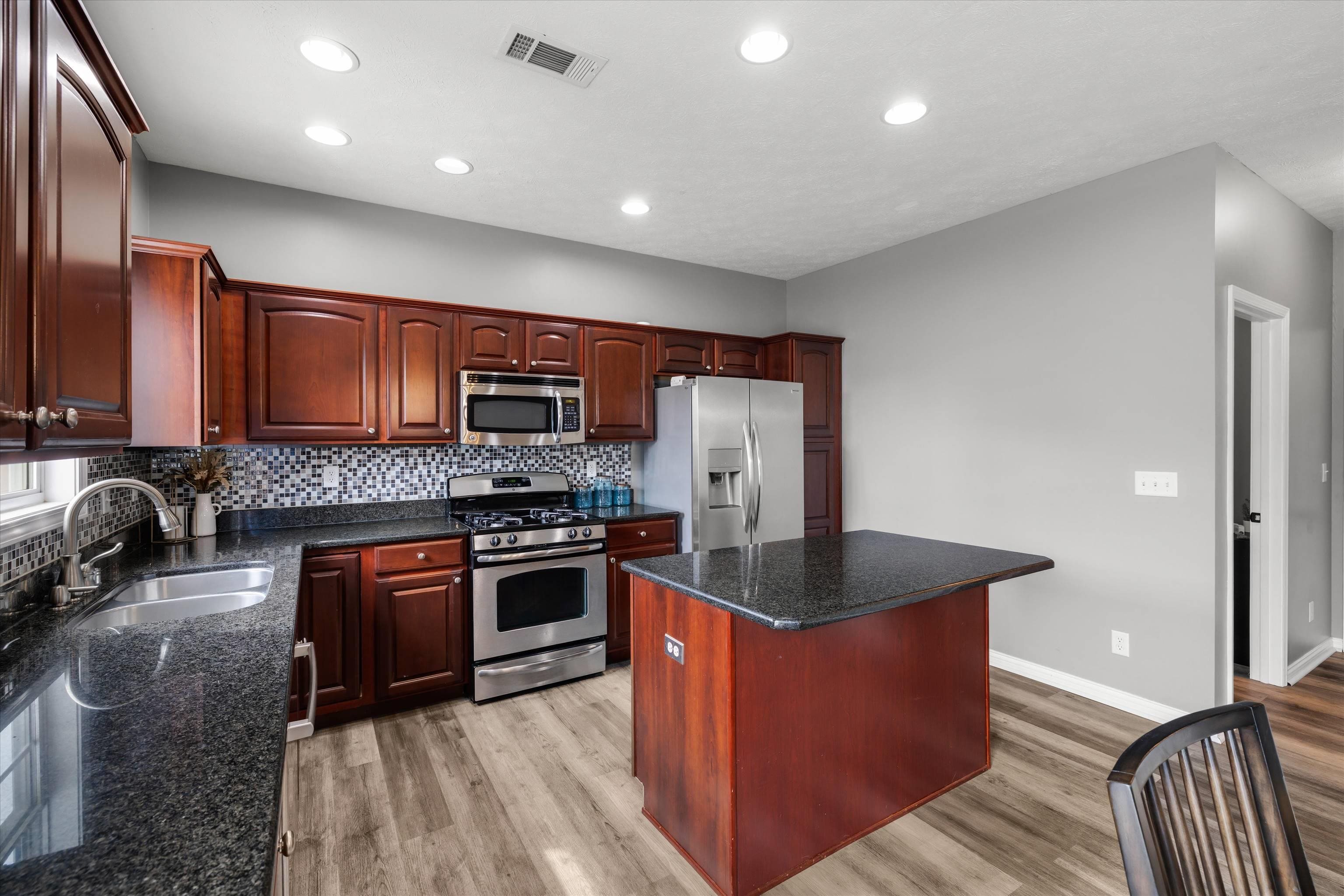 Kitchen with cherry cabinets, black granite counters, a central island, and stainless steel appliances.
