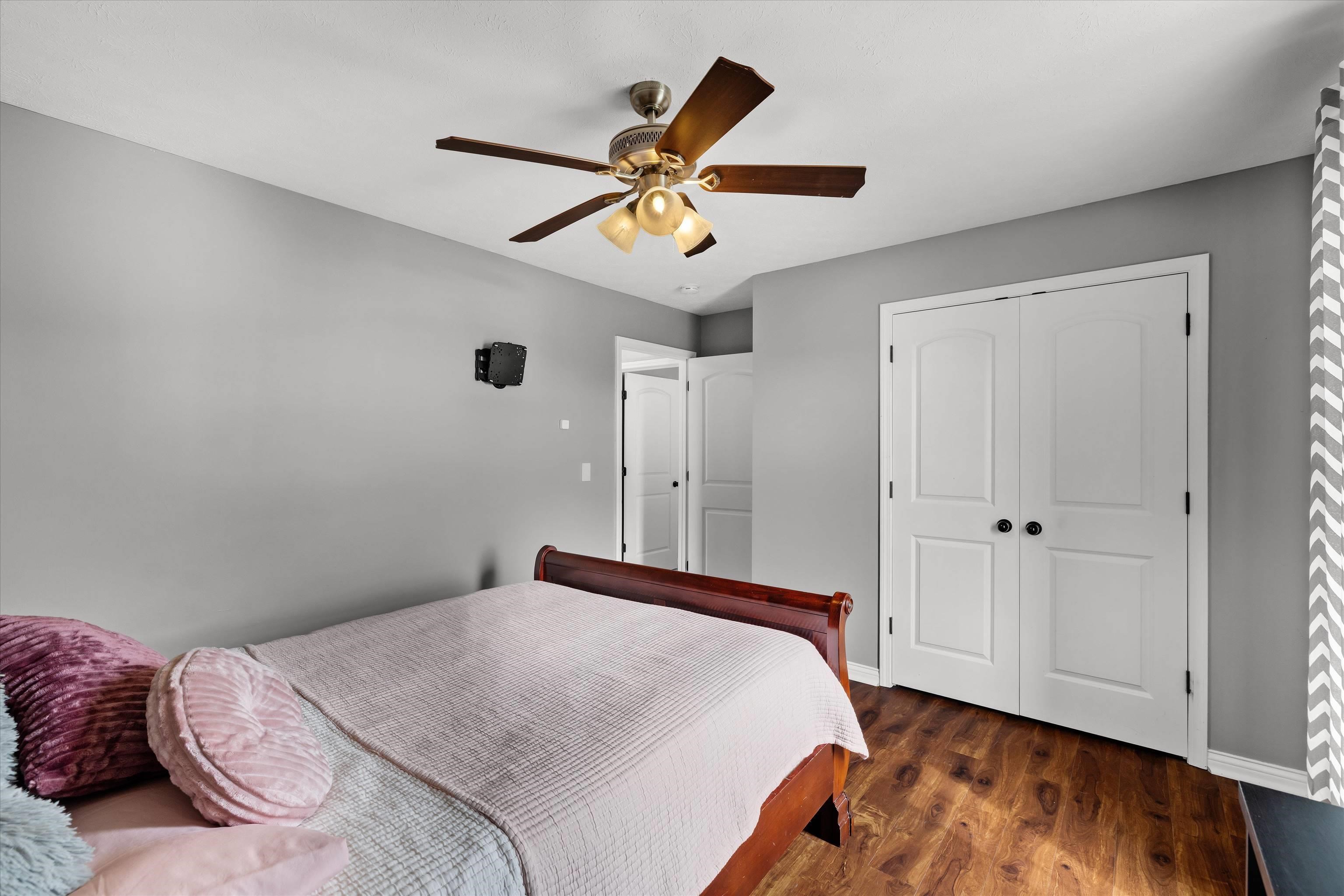Bedroom with a wooden bed, pink pillows, gray walls, and white closet doors.