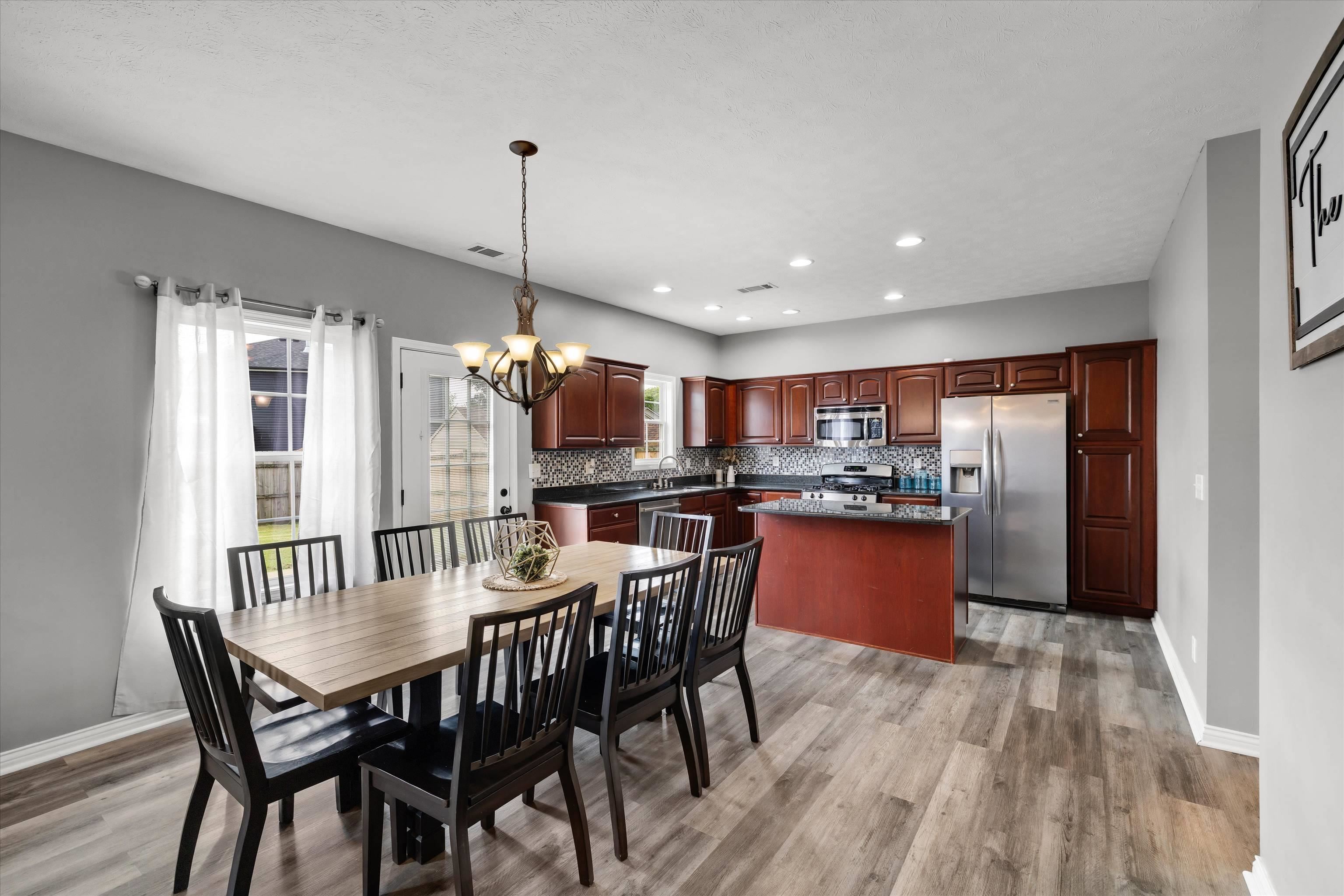 Kitchen and dining area with cherry cabinets, stainless steel appliances, and a table beside tall curtained windows.