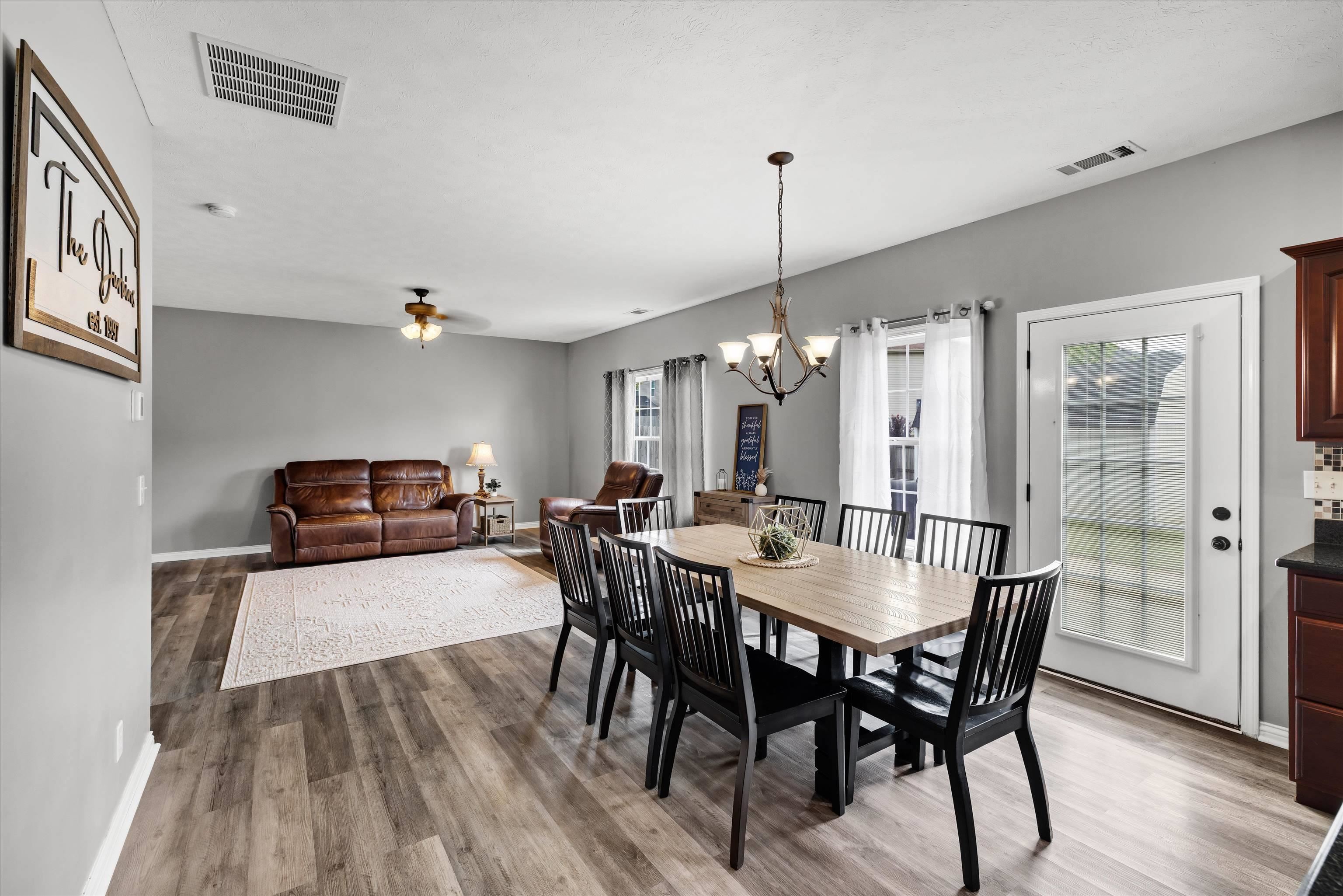 Open dining and living area with a long wood table, black chairs, and brown leather seating.