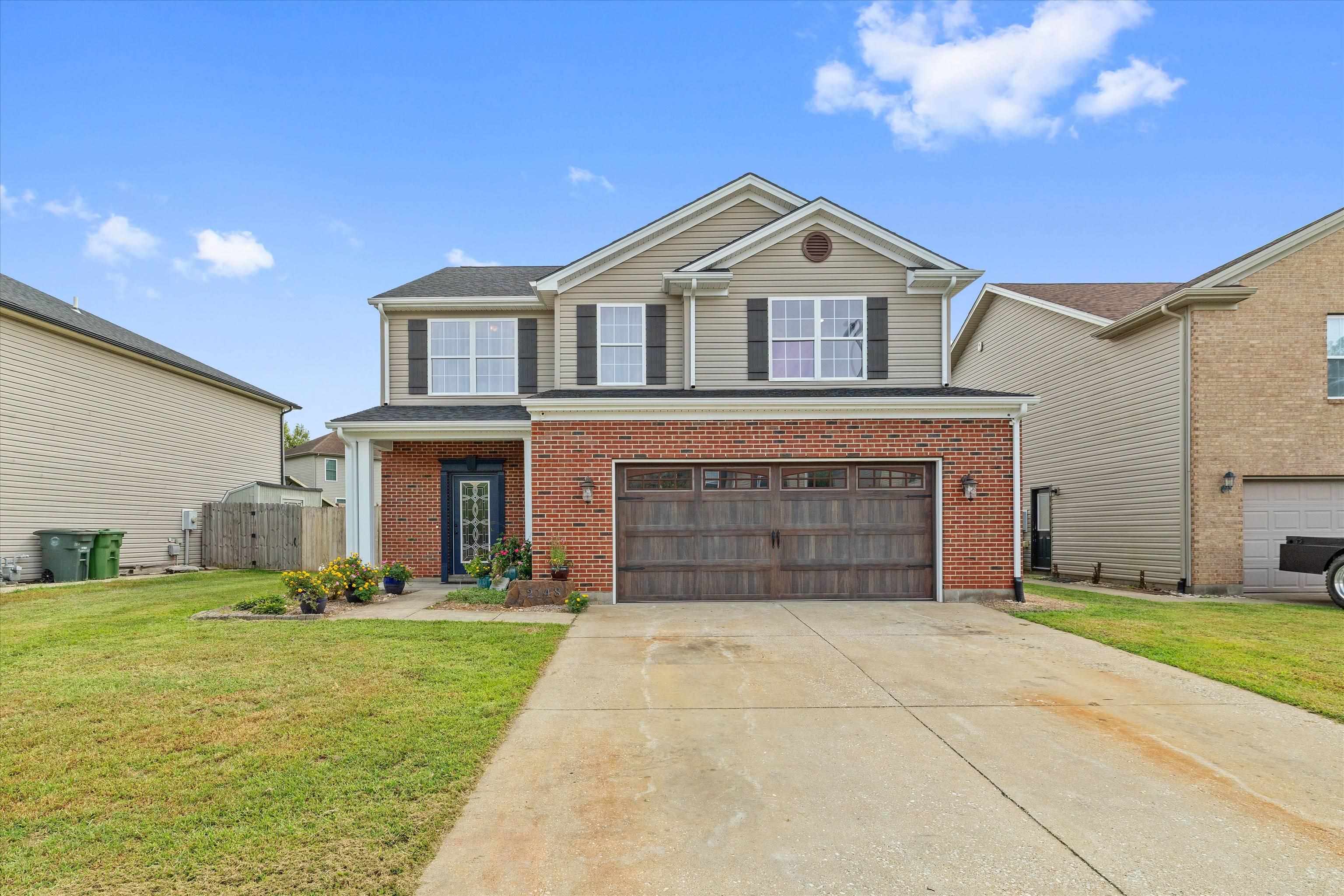 Two-story brick-and-siding home with a dark double garage door and flower beds by the entrance.