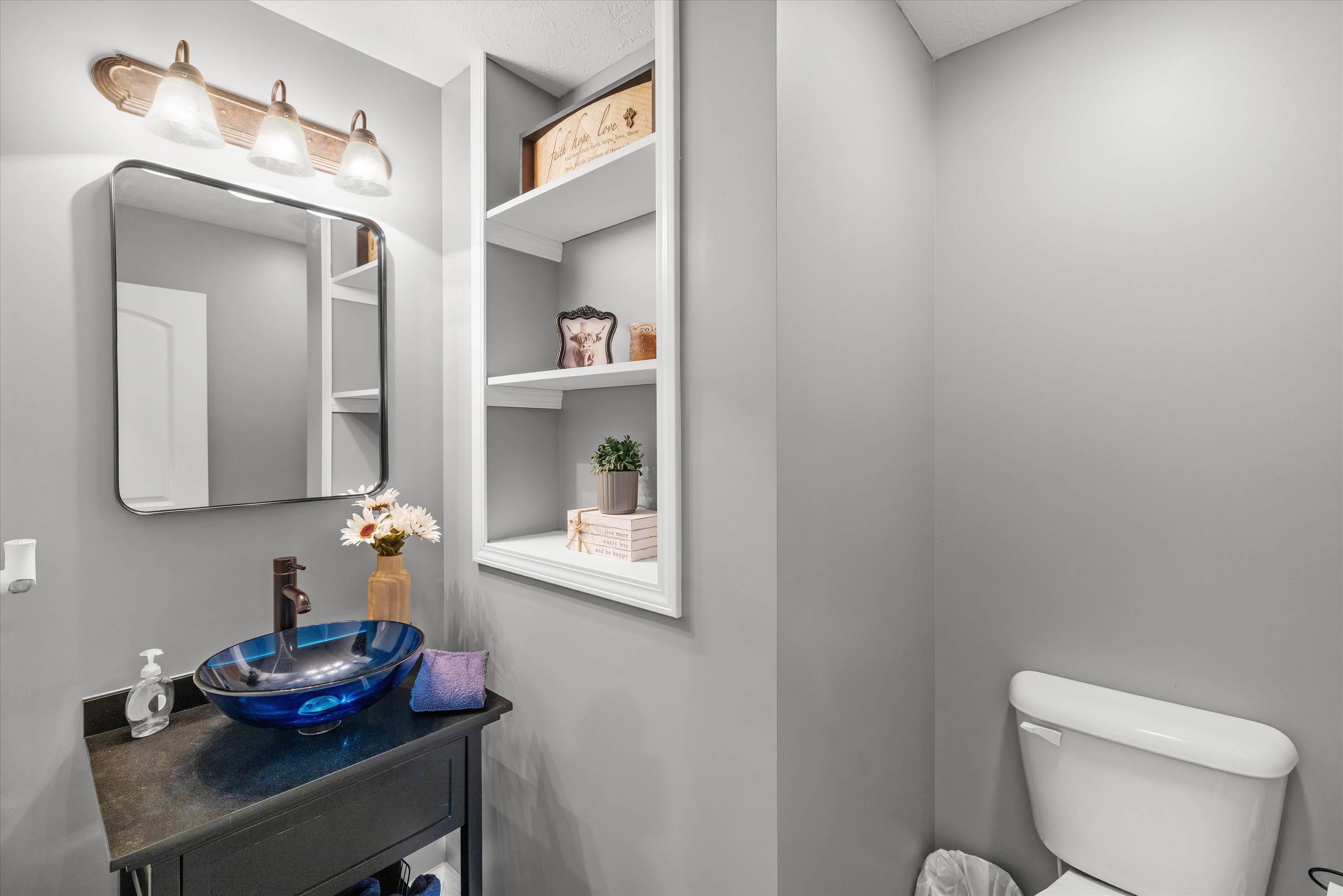 Powder room with a blue glass vessel sink, dark vanity, built-in shelves, and white toilet.