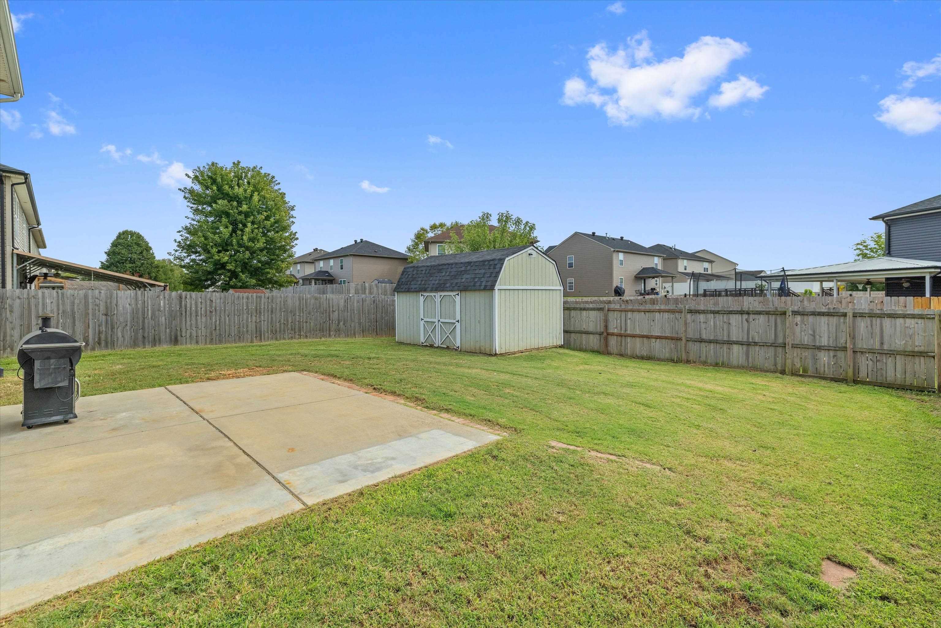 Fenced backyard with a storage shed, broad lawn, and concrete patio.