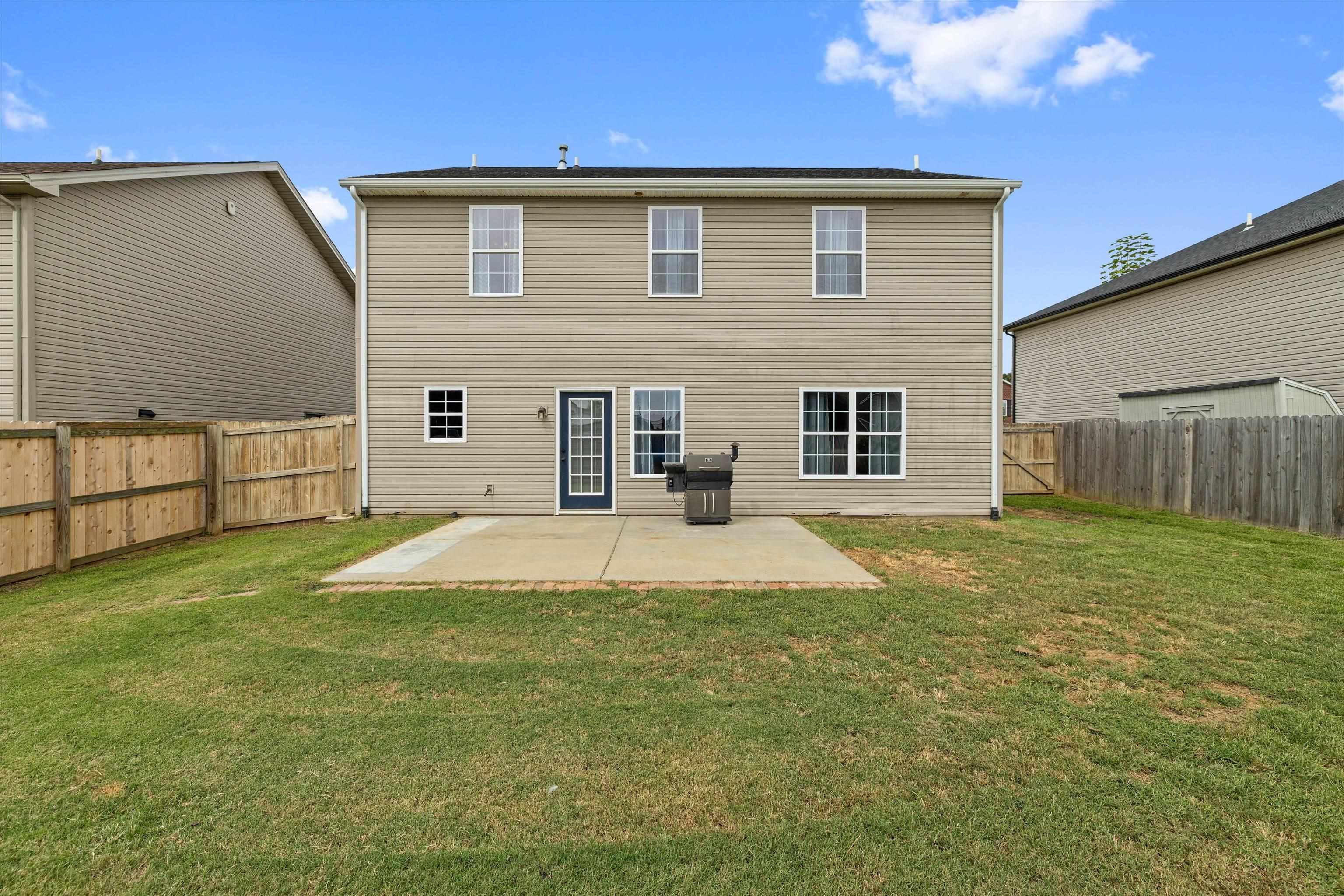 Rear of a two-story beige house with a fenced lawn and concrete patio.