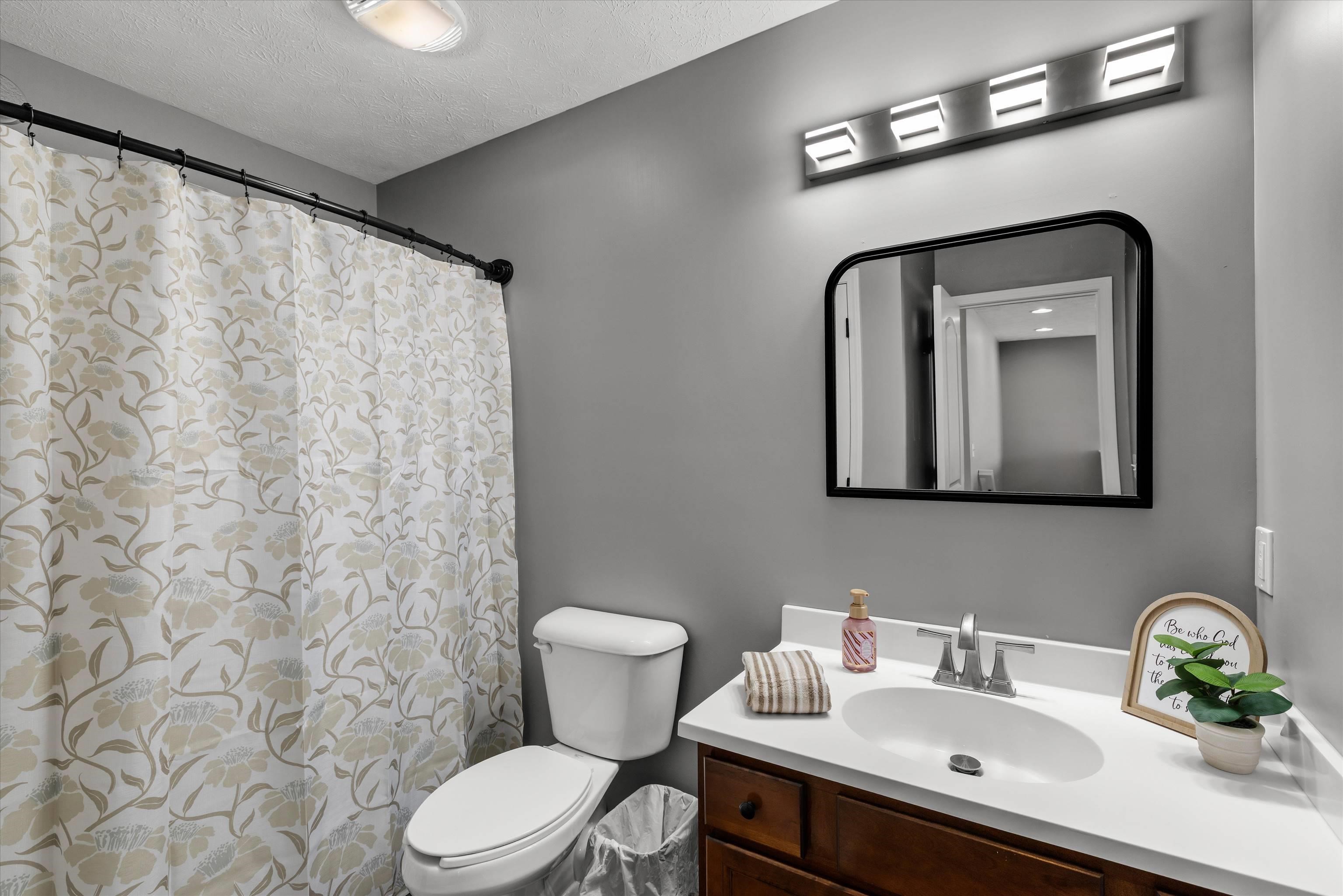 Bathroom with a floral shower curtain and dark wood vanity beneath a black-framed mirror.