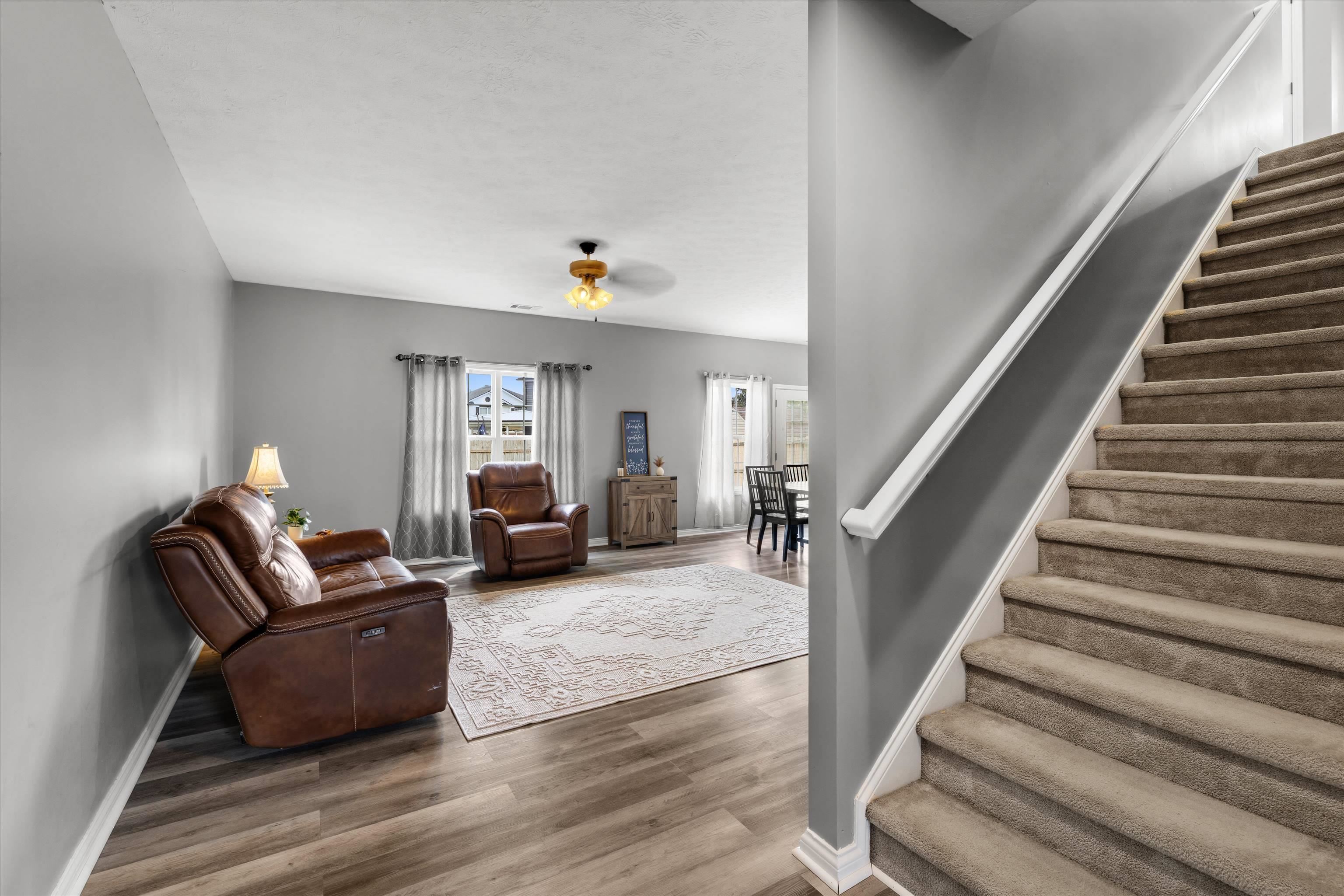 Living room with brown leather seating and patterned rug beside a carpeted staircase.