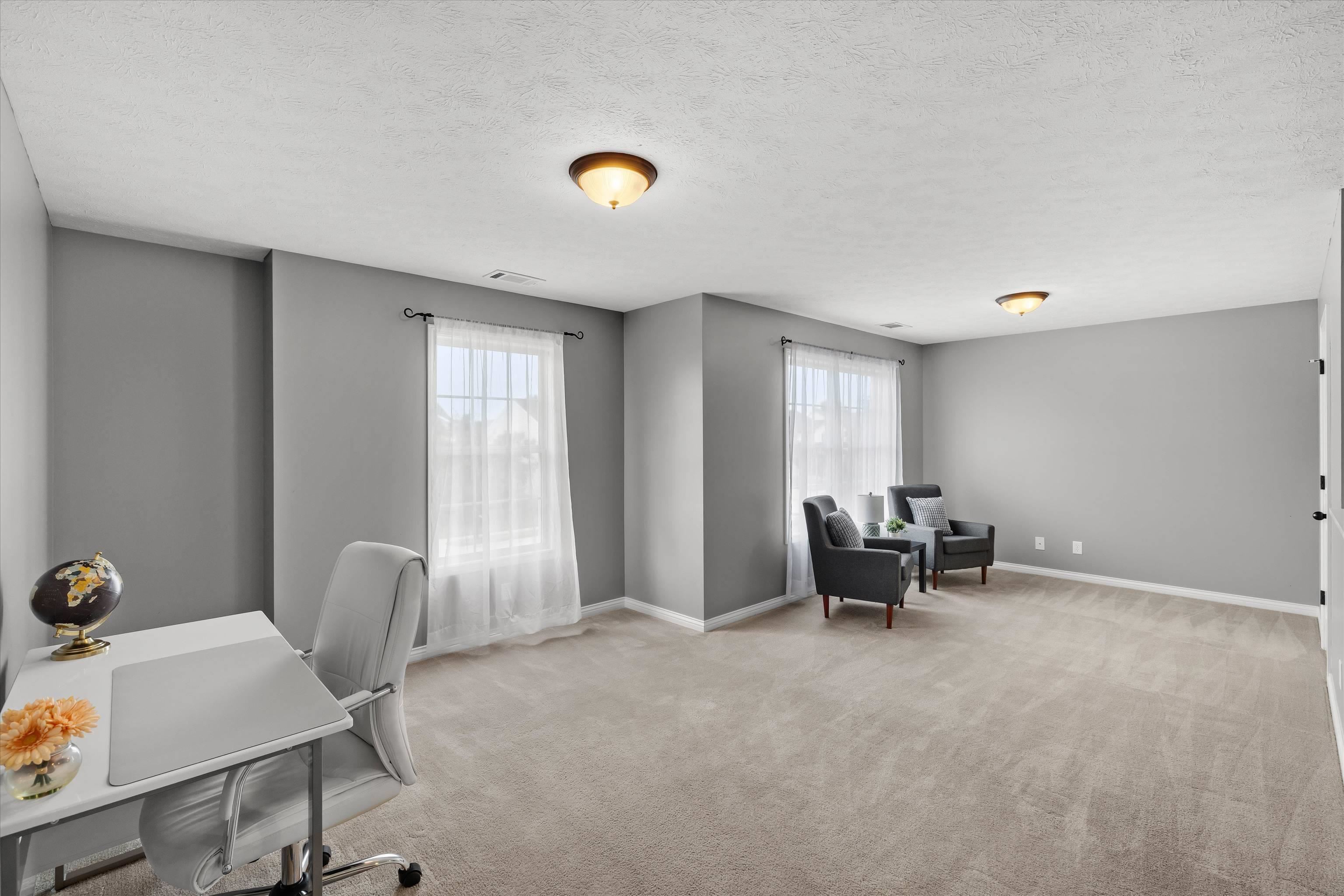 Spacious gray room with a white desk and chair, two curtained windows, and a pair of dark armchairs.