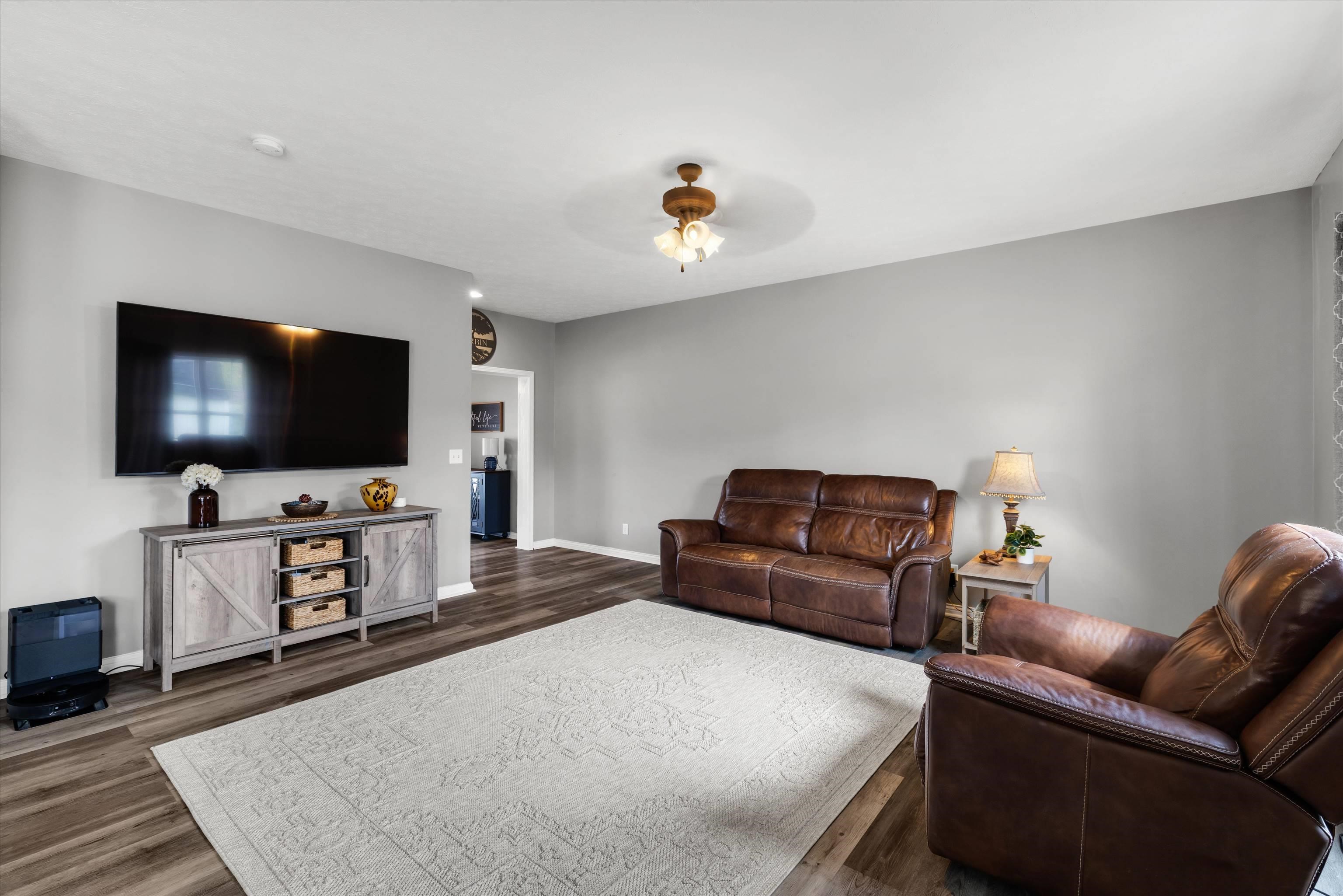 Furnished living room with brown leather sofas, a large white rug, and a wall-mounted television.