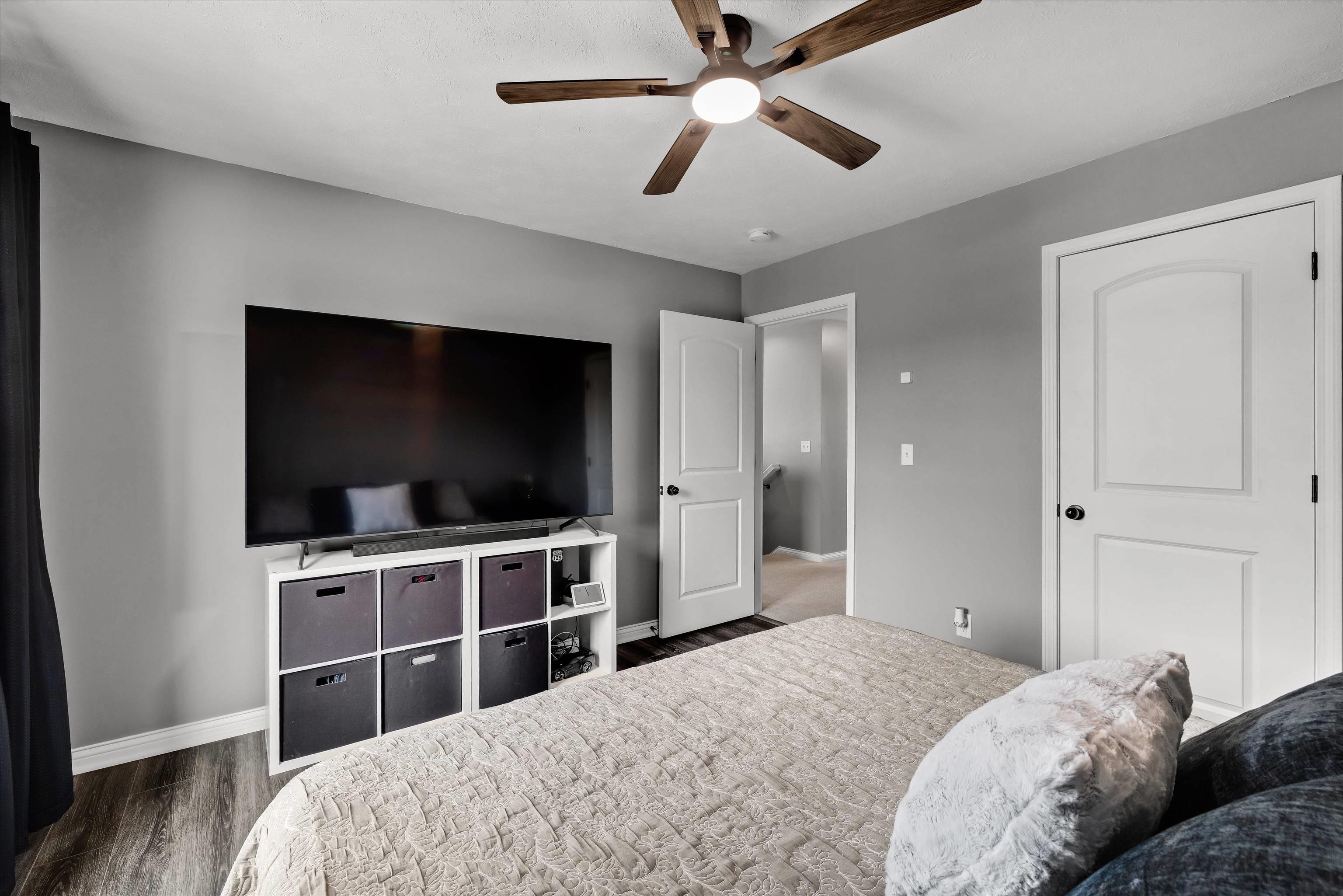 Furnished bedroom with a large television on a cubby unit and a wood-blade ceiling fan.