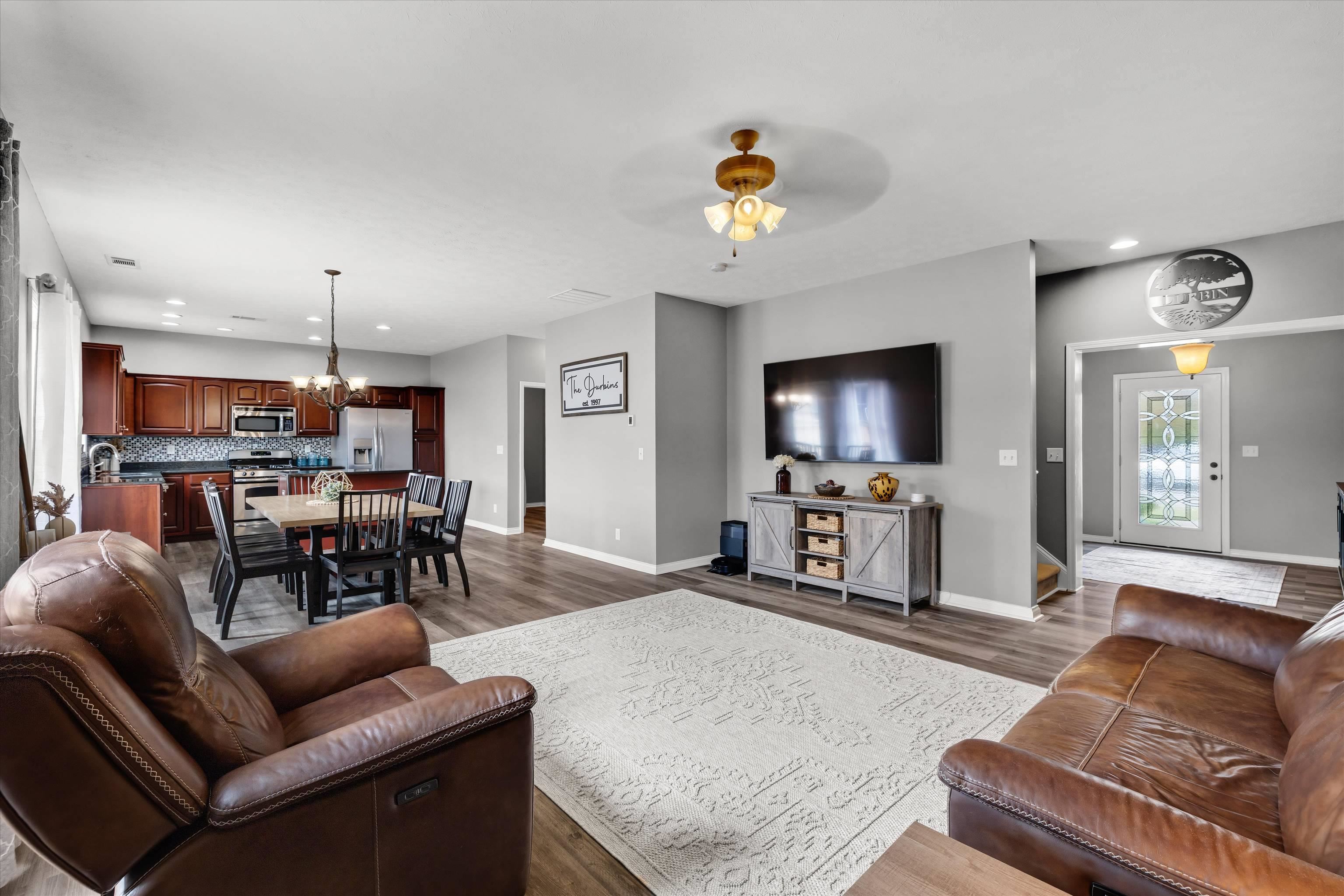 Open-concept living room with brown leather sofas, dining table, and dark wood kitchen cabinets.