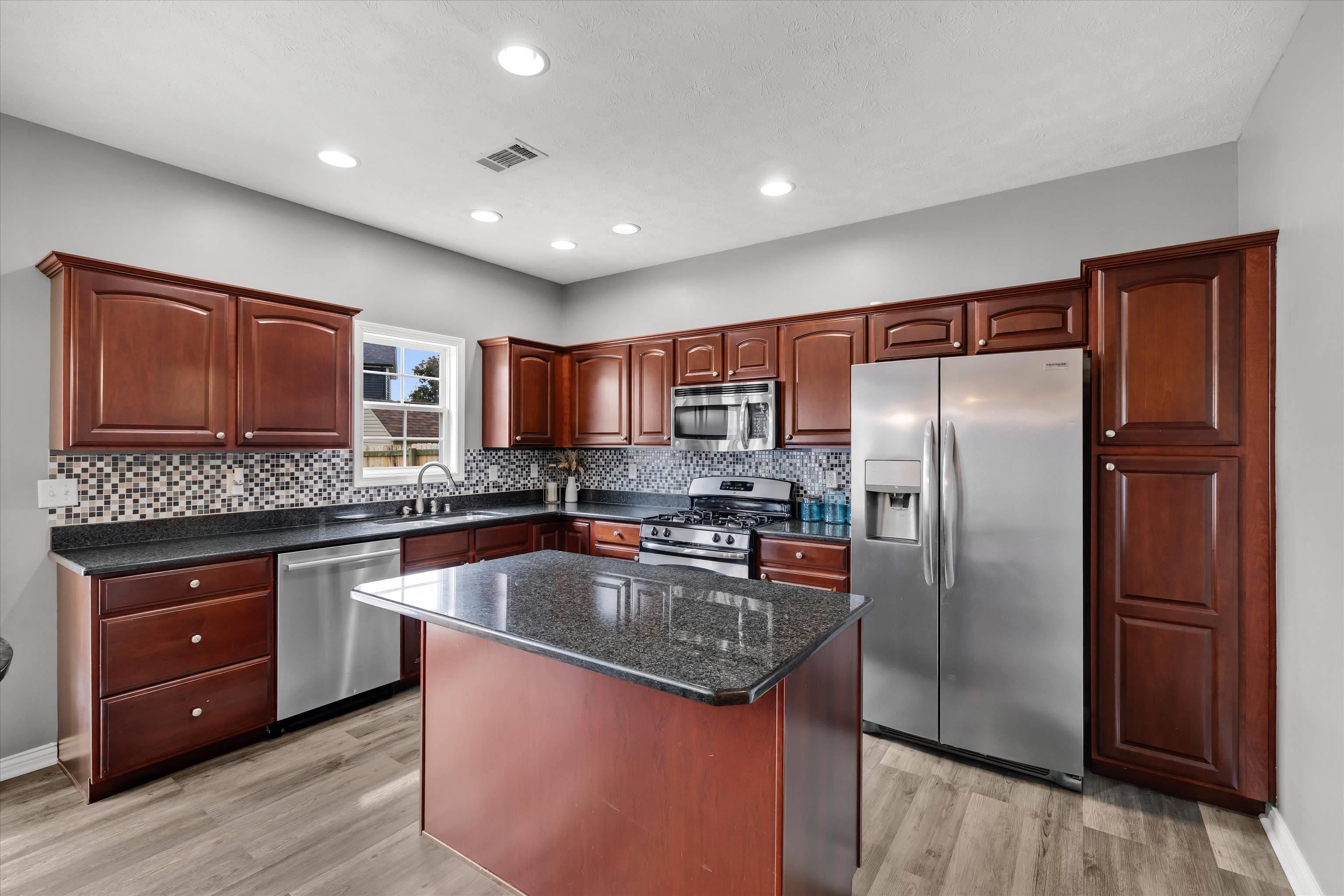 Kitchen with dark wood cabinets, granite island, stainless steel appliances, and tiled backsplash.