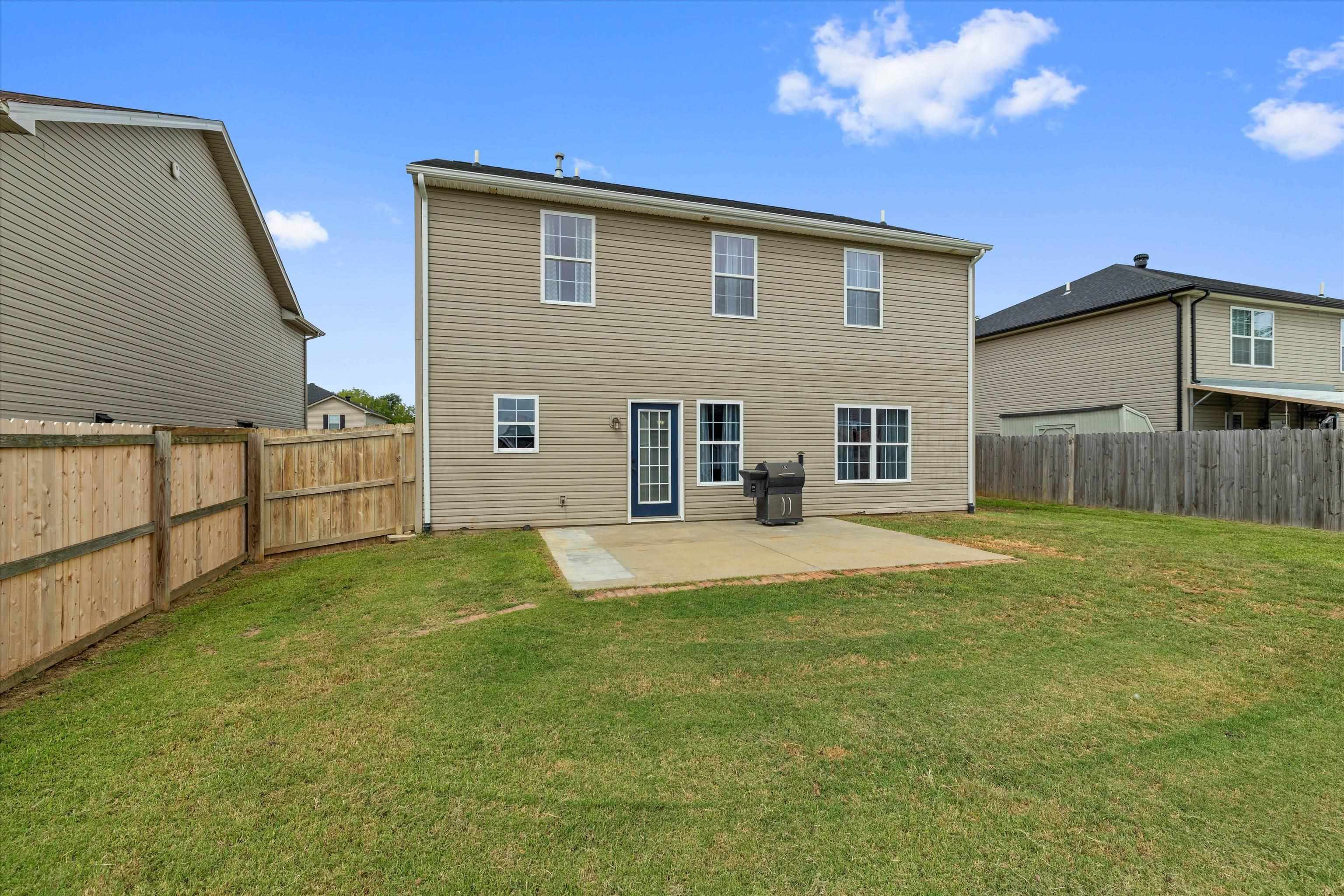 Two-story home with a fenced backyard, concrete patio, and grill.
