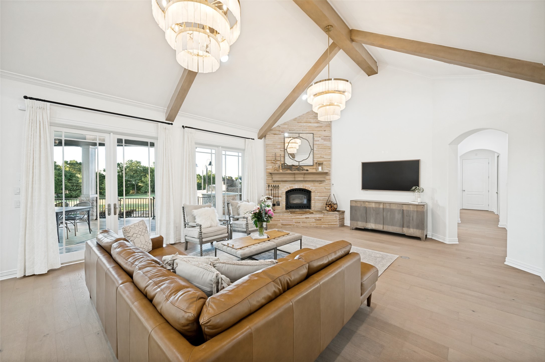 Living room with vaulted wood-beam ceiling, brick fireplace, leather sectional, and glass doors to a patio.