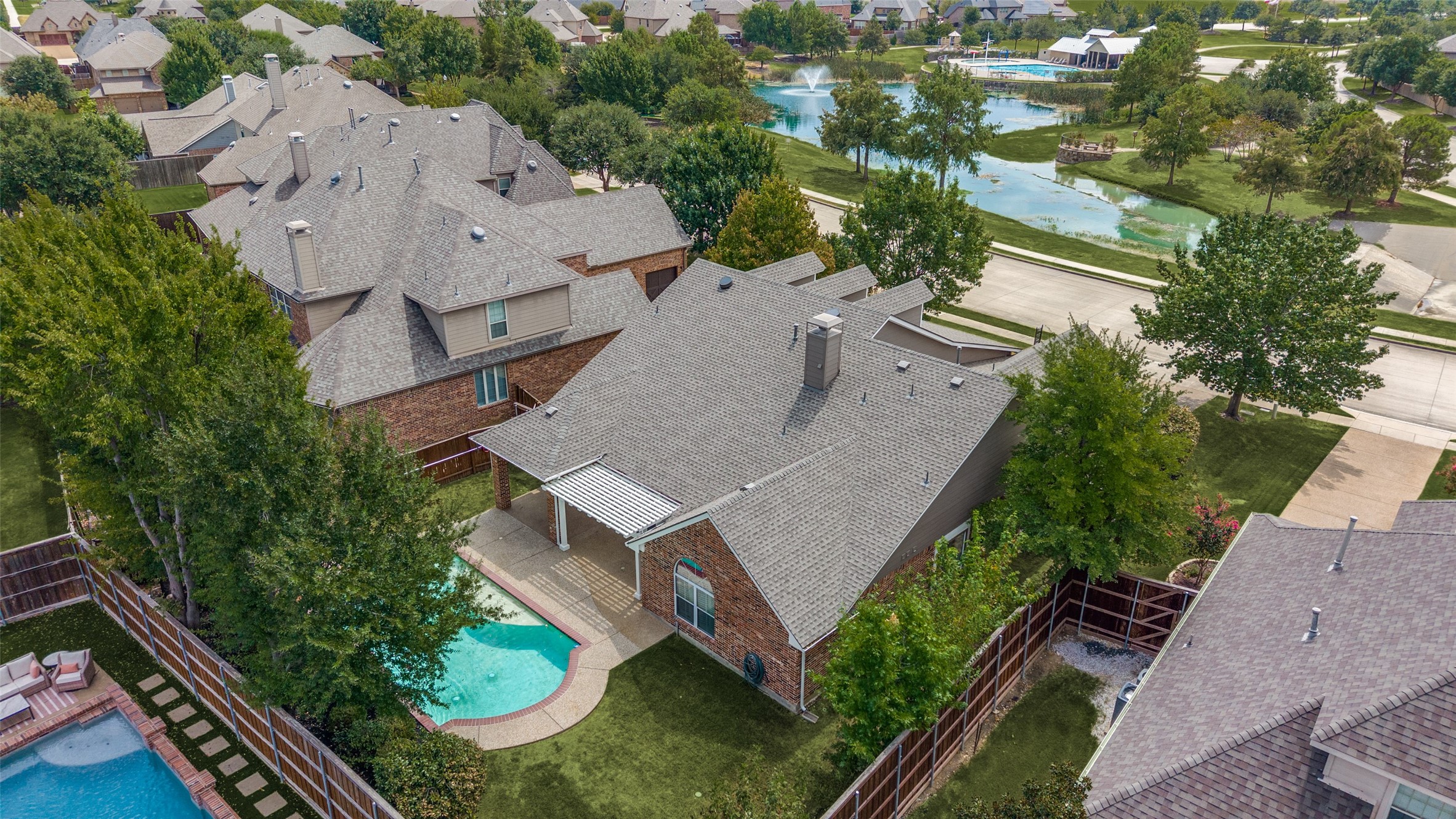 Aerial view of a brick home with a curved backyard pool and a pond with fountain nearby.