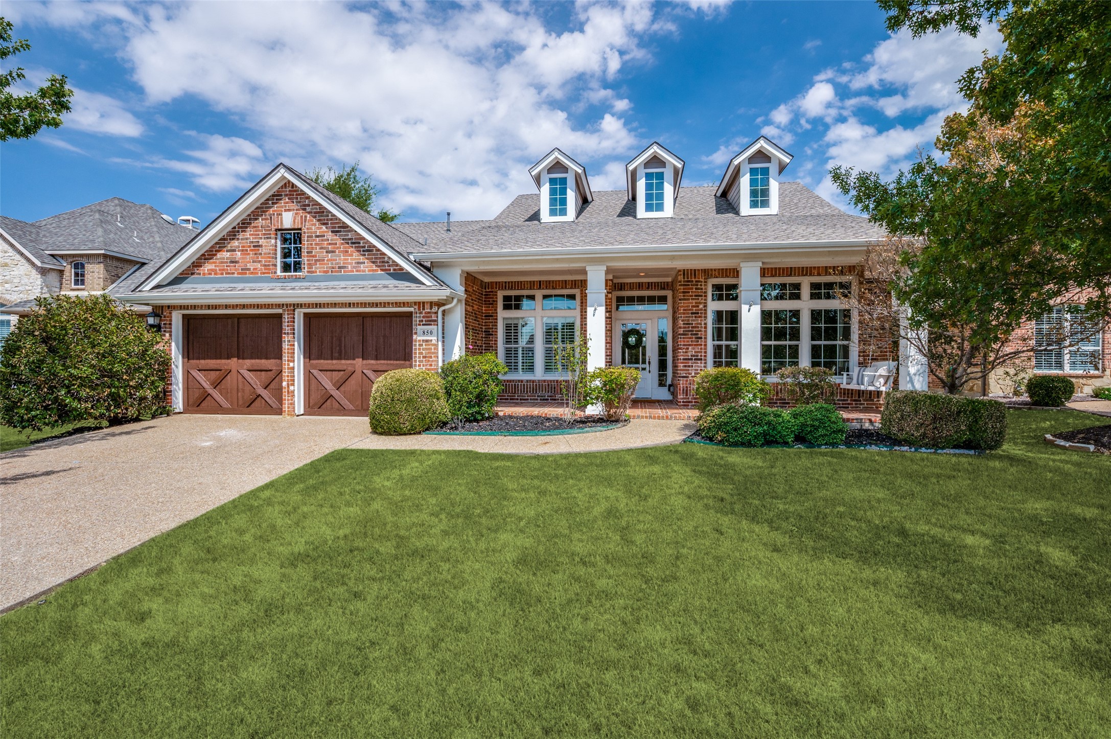 Red-brick house with three roof dormers, double garage, and broad front lawn.