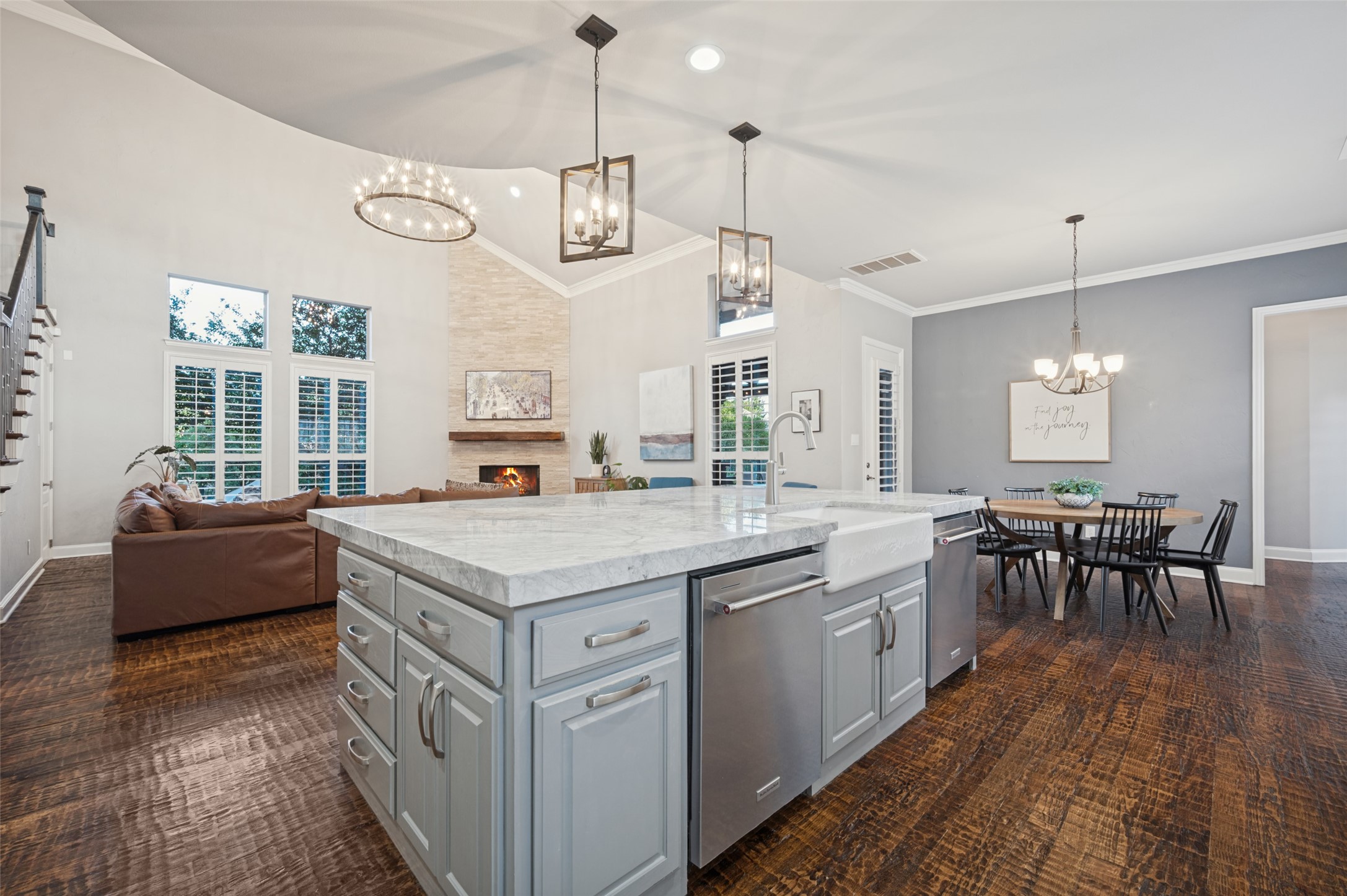 Open-plan kitchen with a large marble island, adjoining living area, stone fireplace, and dining table.