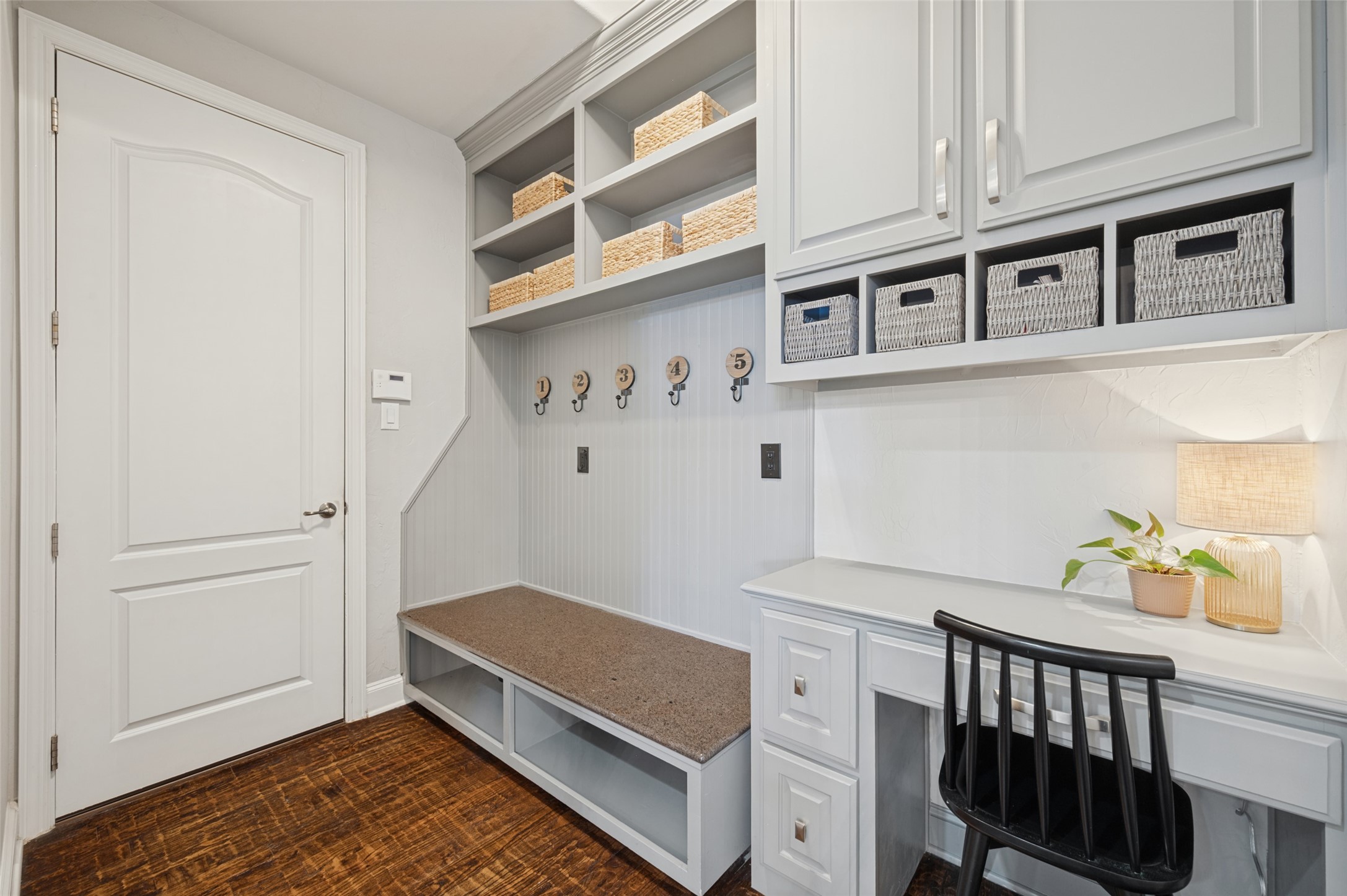 Mudroom with white built-in storage, woven baskets, a cushioned bench, and numbered hooks.