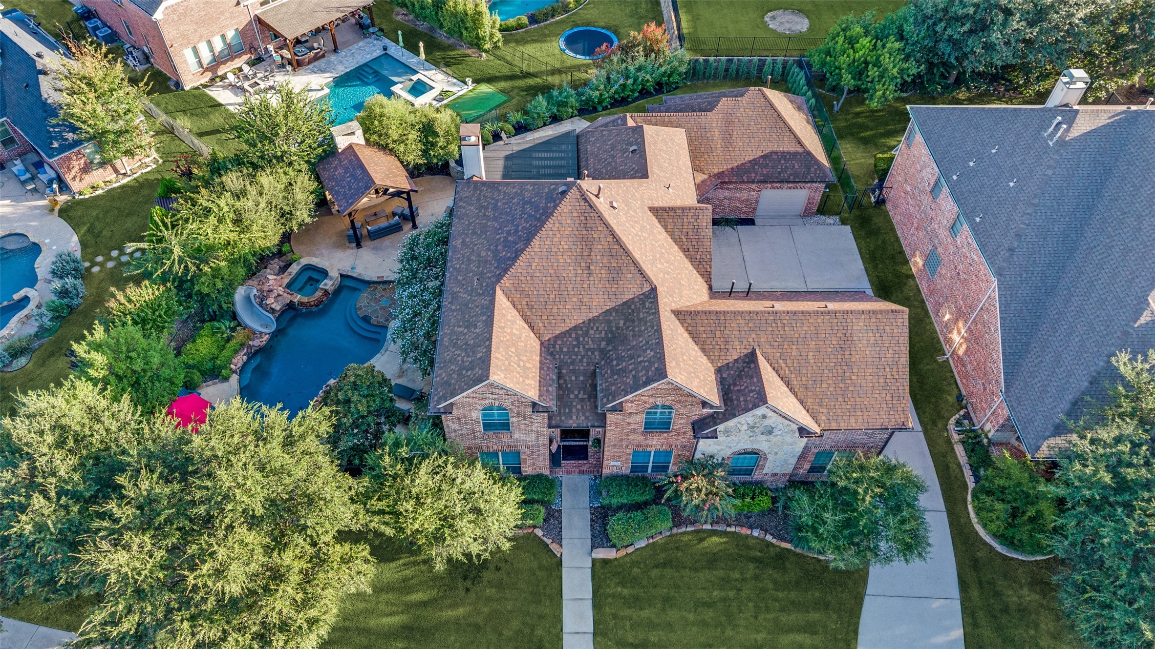 Aerial view of a brick house with a backyard pool, spa, and covered patio.