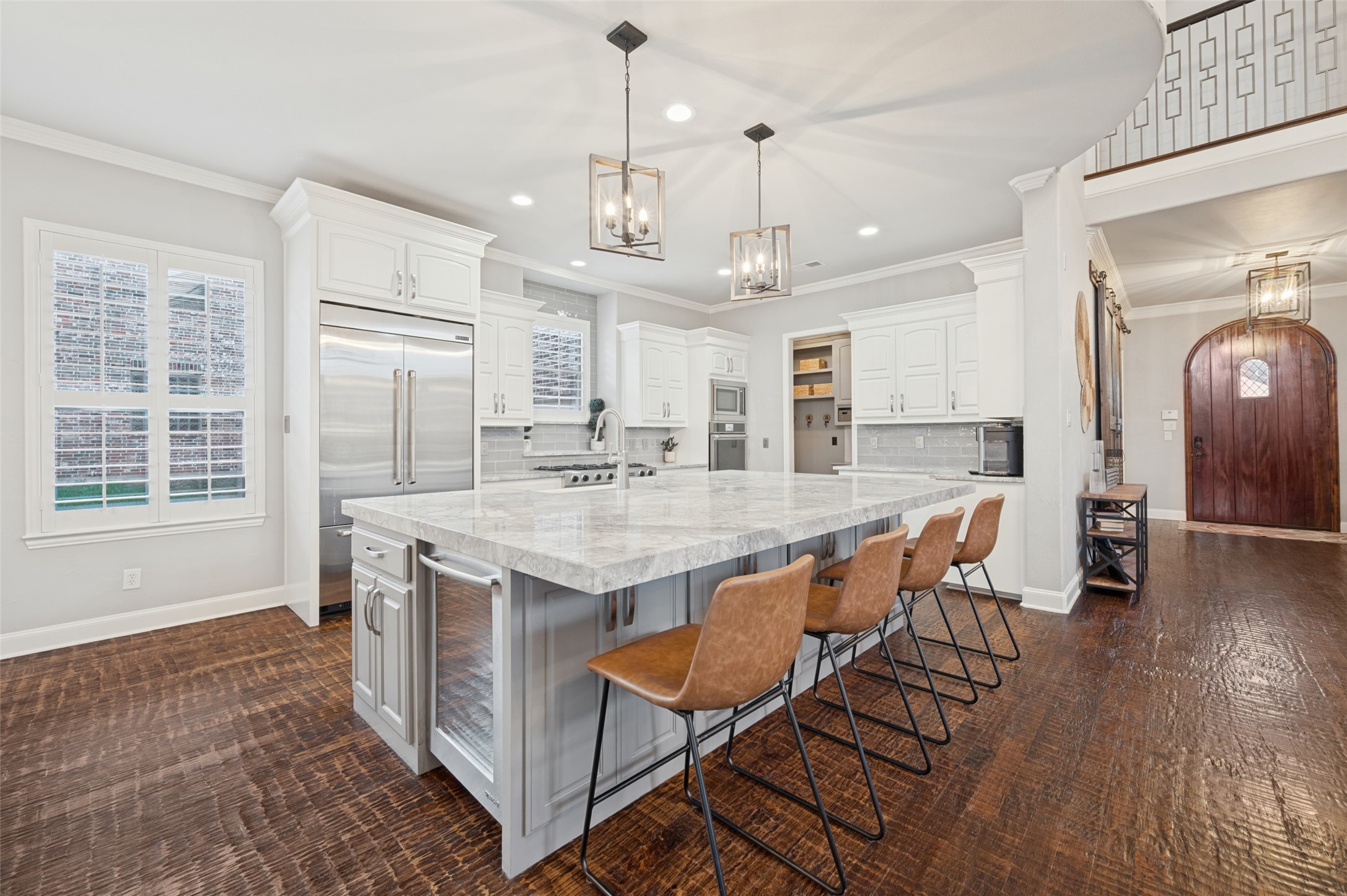 Kitchen with a large stone island, four tan bar stools, white cabinets and dark wood floors.