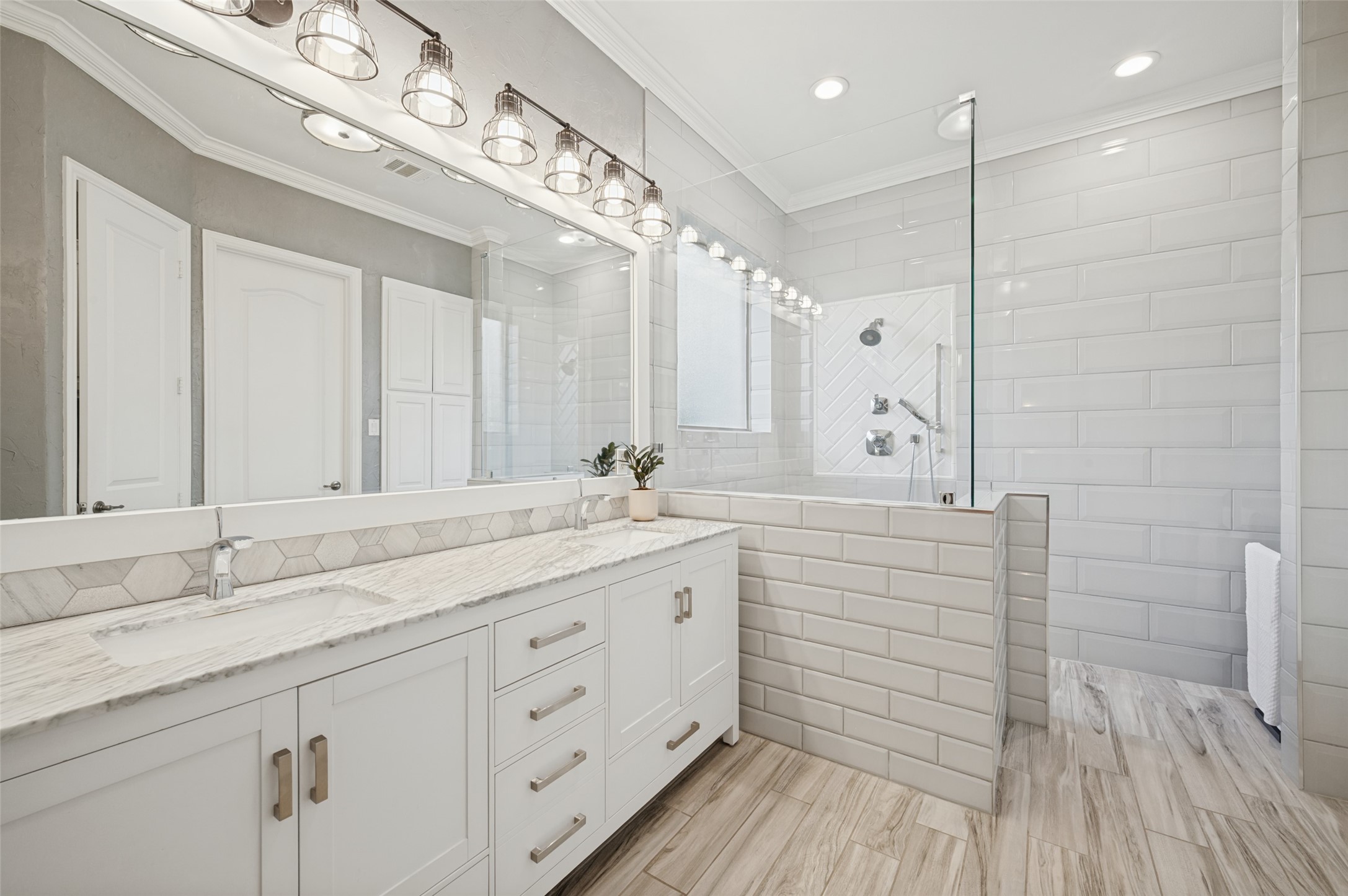 Bathroom with a long white vanity and glass shower featuring white subway tile and a herringbone accent niche.